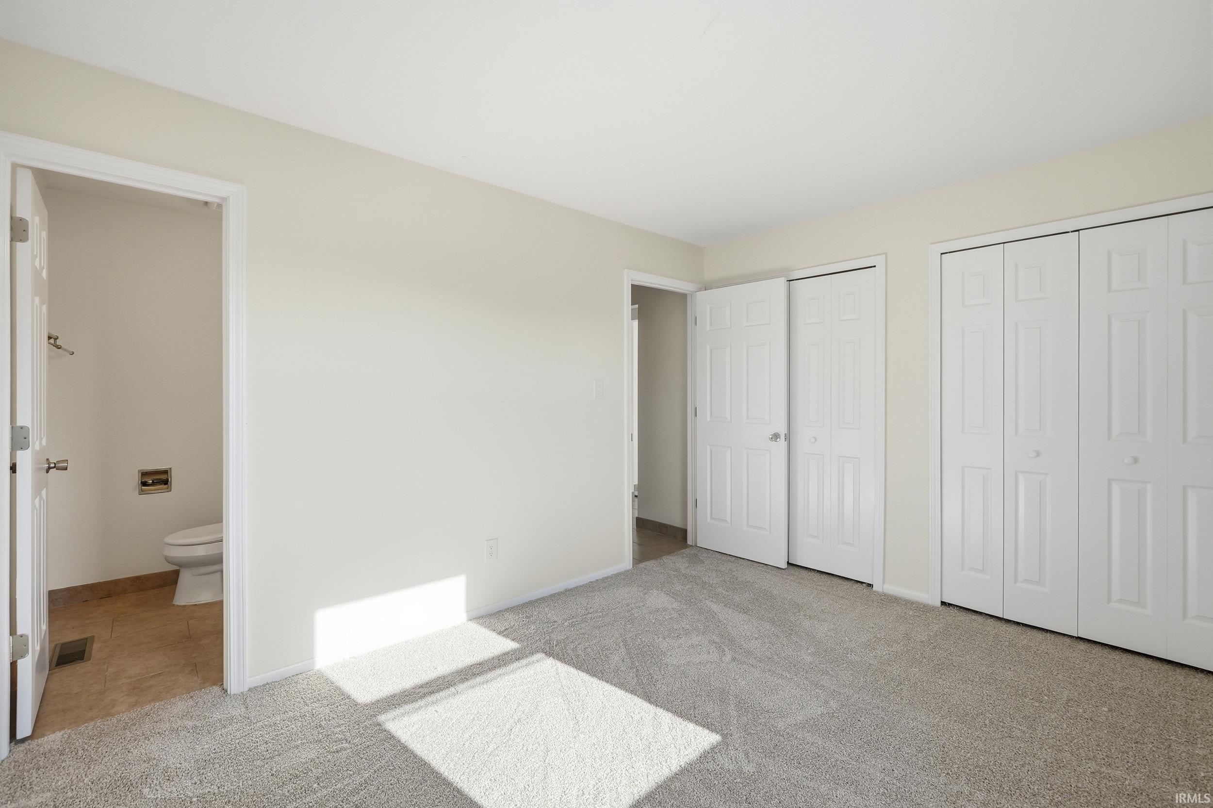 Unfurnished bedroom featuring light colored carpet, two closets, connected bathroom, and light tile patterned flooring