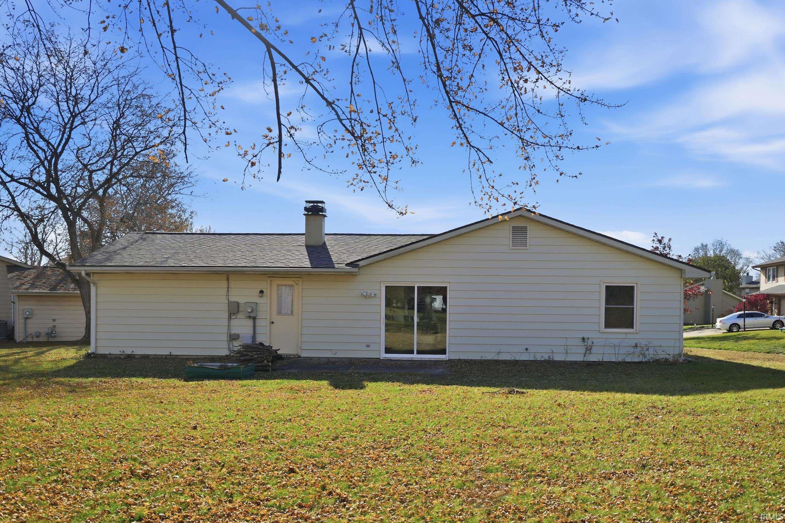 Rear view of property featuring a yard, a chimney, and roof with shingles