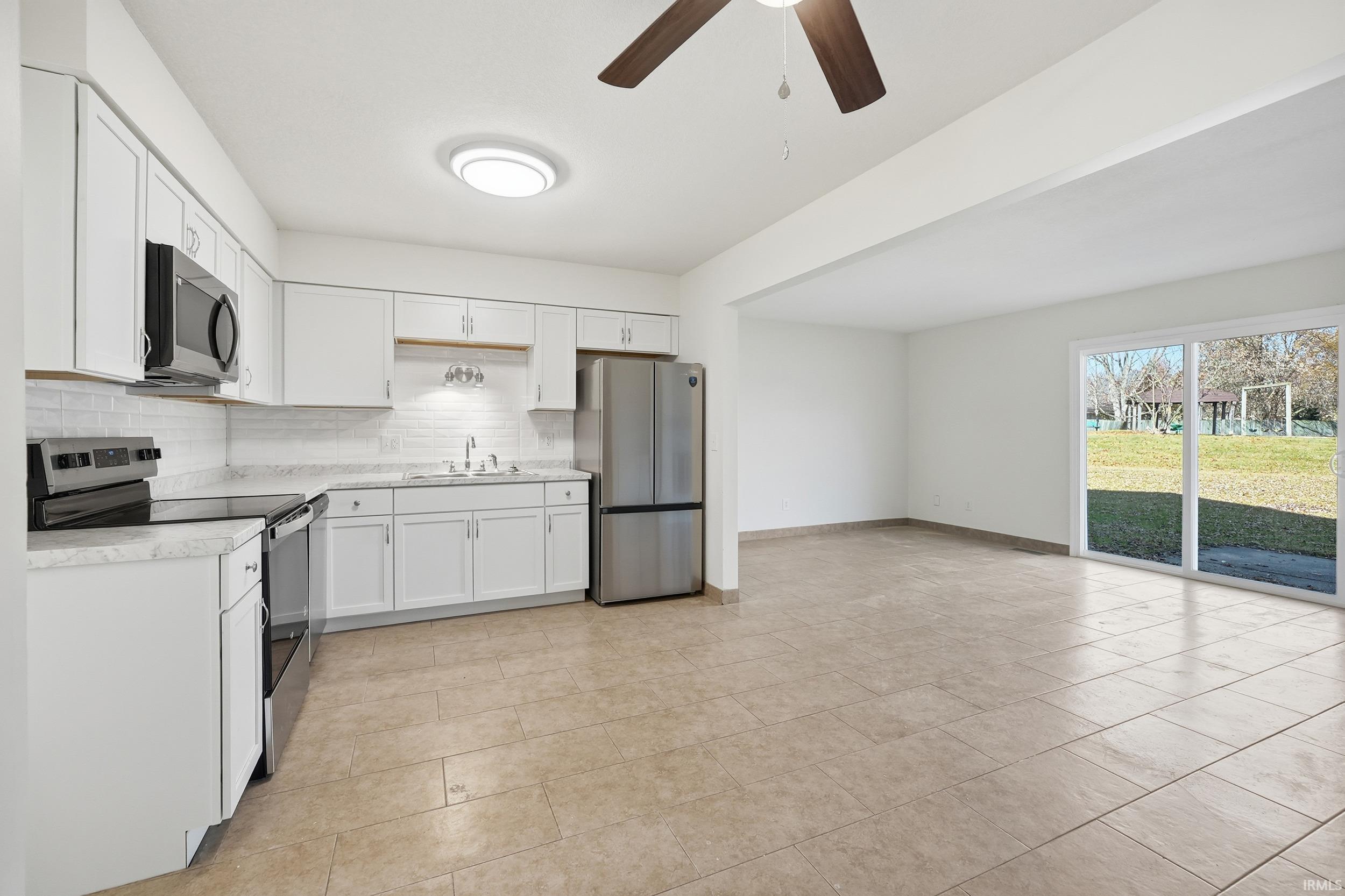 Kitchen featuring appliances with stainless steel finishes, backsplash, light countertops, white cabinets, and a ceiling fan