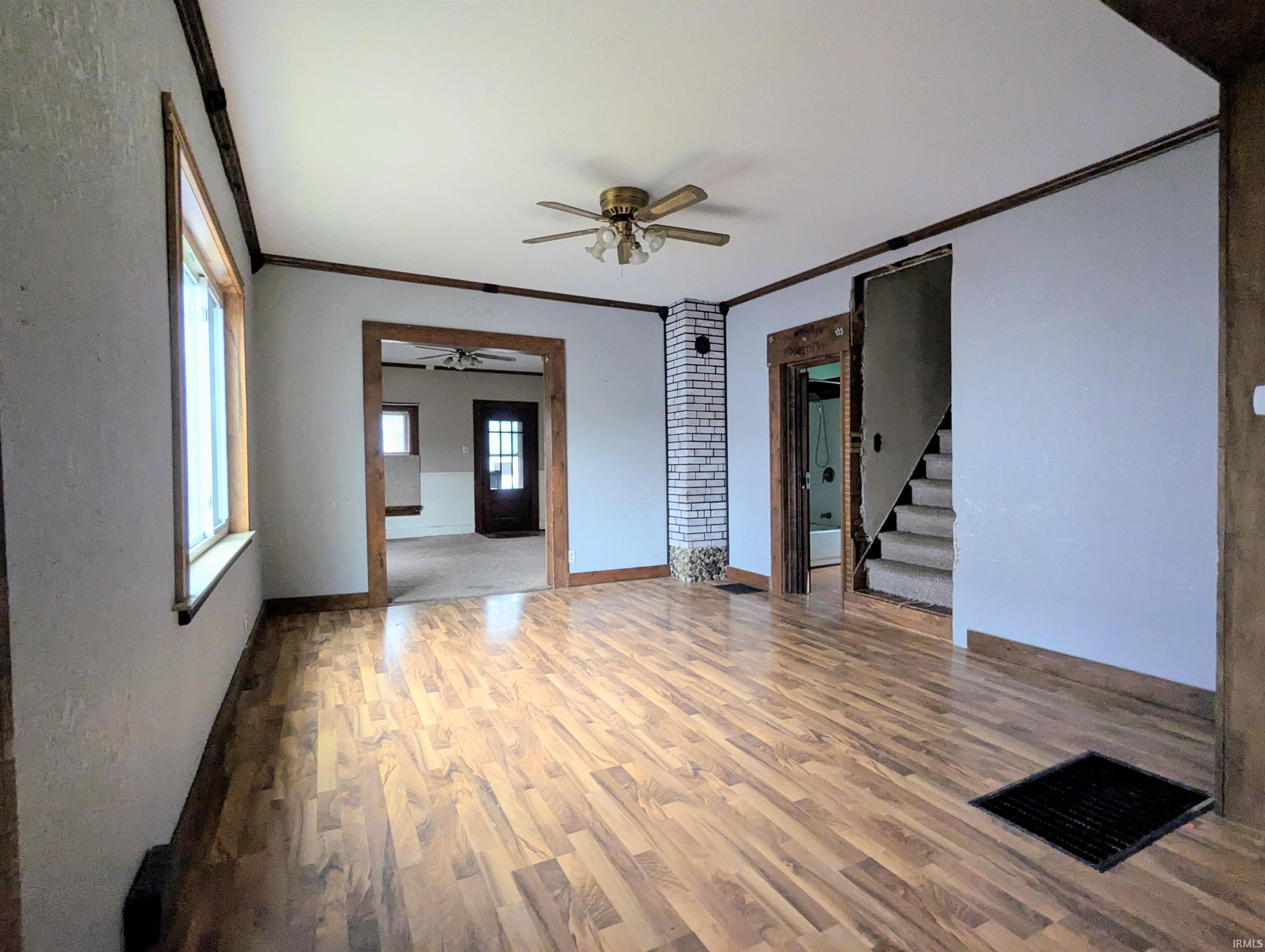Unfurnished room featuring a ceiling fan, ornamental molding, wood finished floors, and stairs