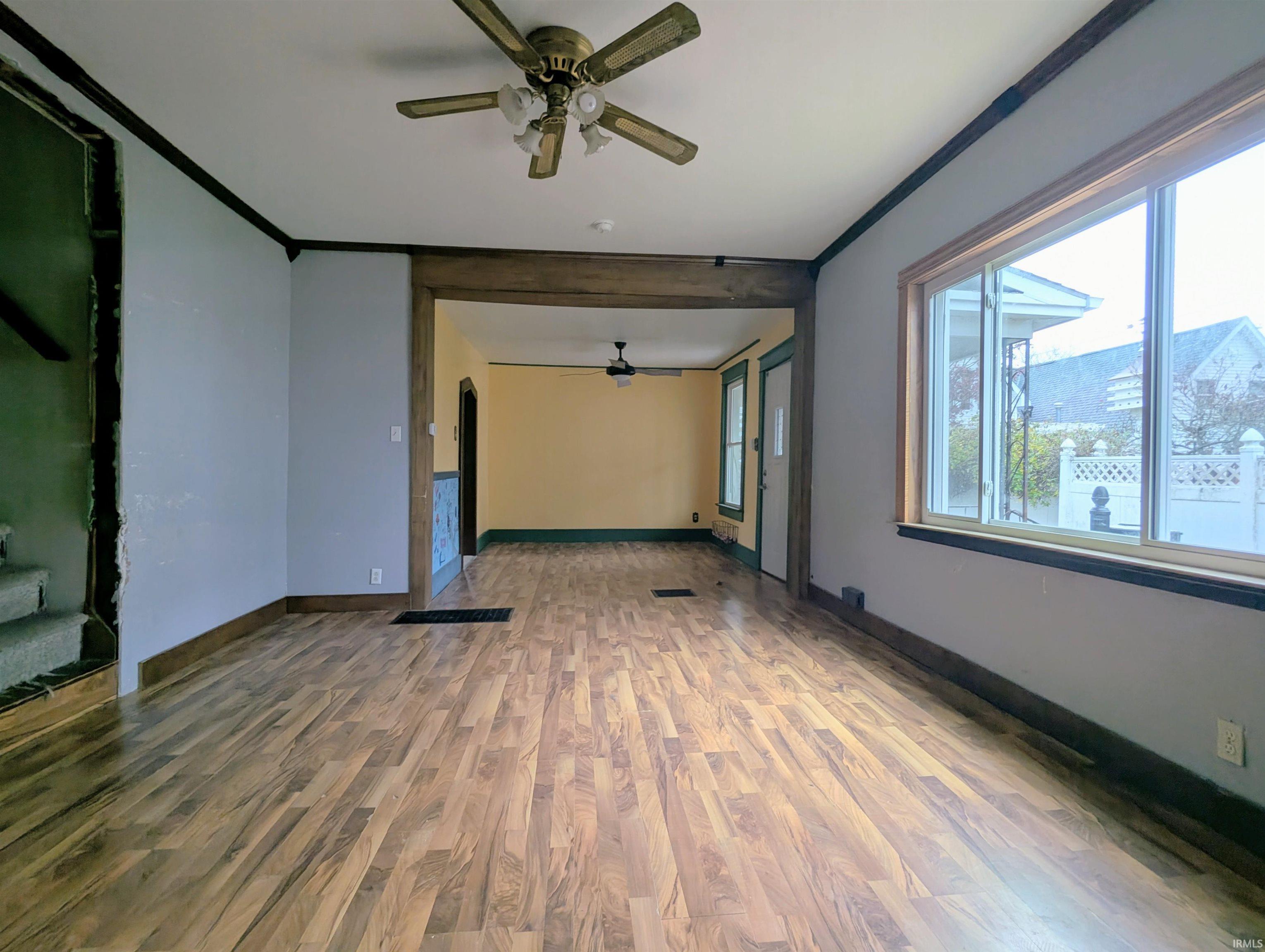 Empty room with wood finished floors, ceiling fan, arched walkways, and crown molding