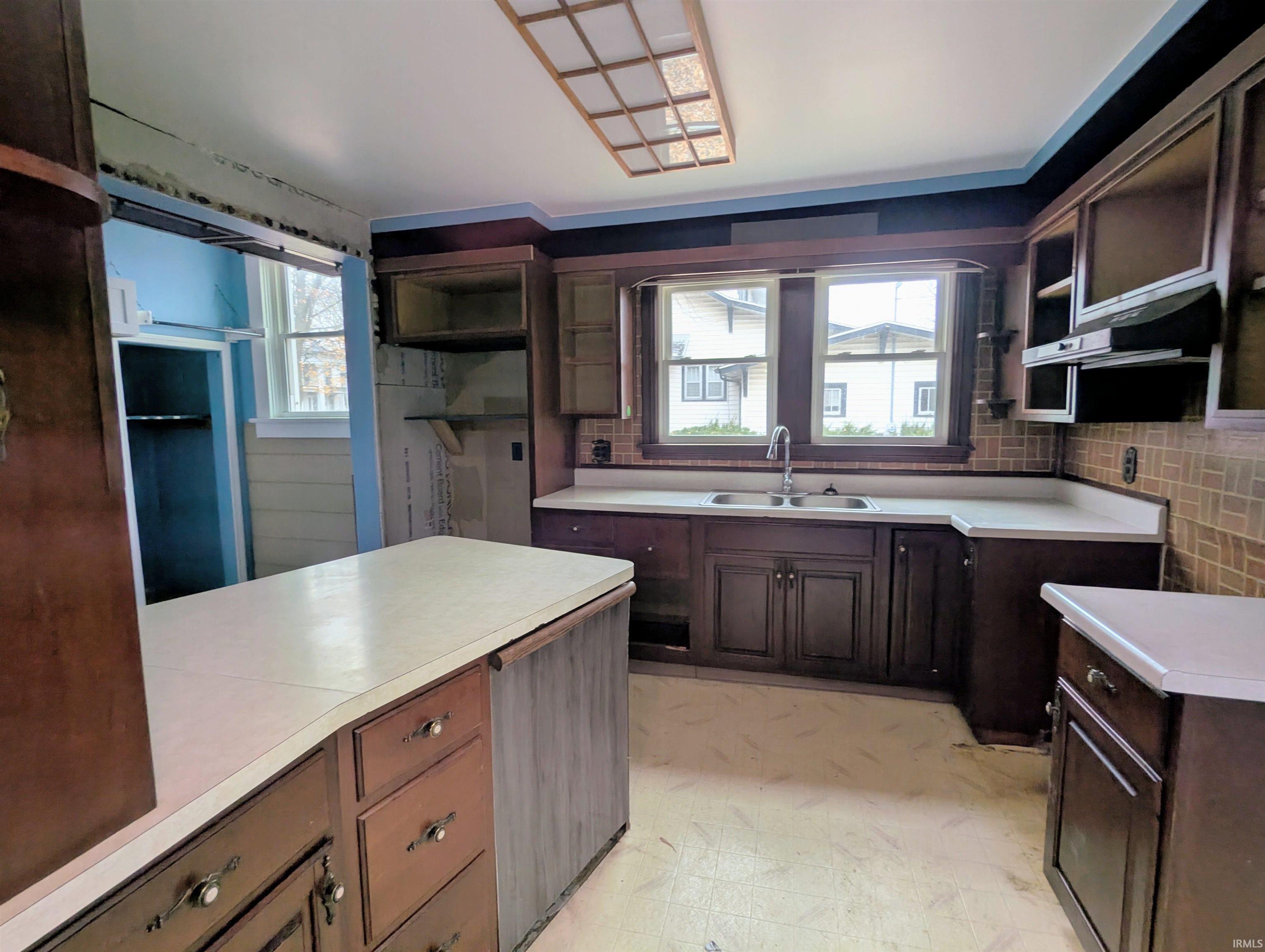 Kitchen featuring open shelves, light flooring, light countertops, dark brown cabinets, and under cabinet range hood