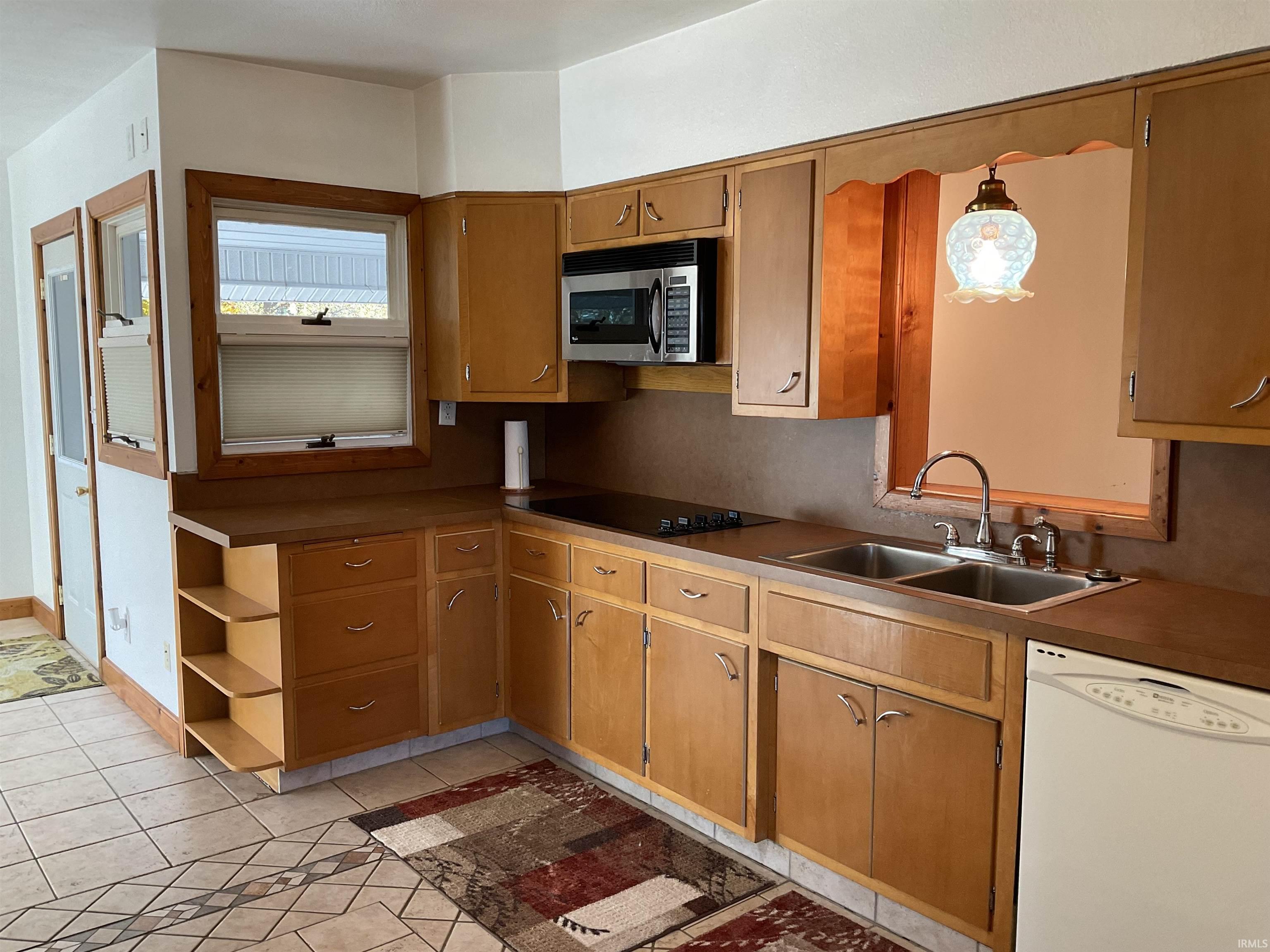 Kitchen featuring white dishwasher, light tile patterned floors, stainless steel microwave, brown cabinets, and black electric cooktop