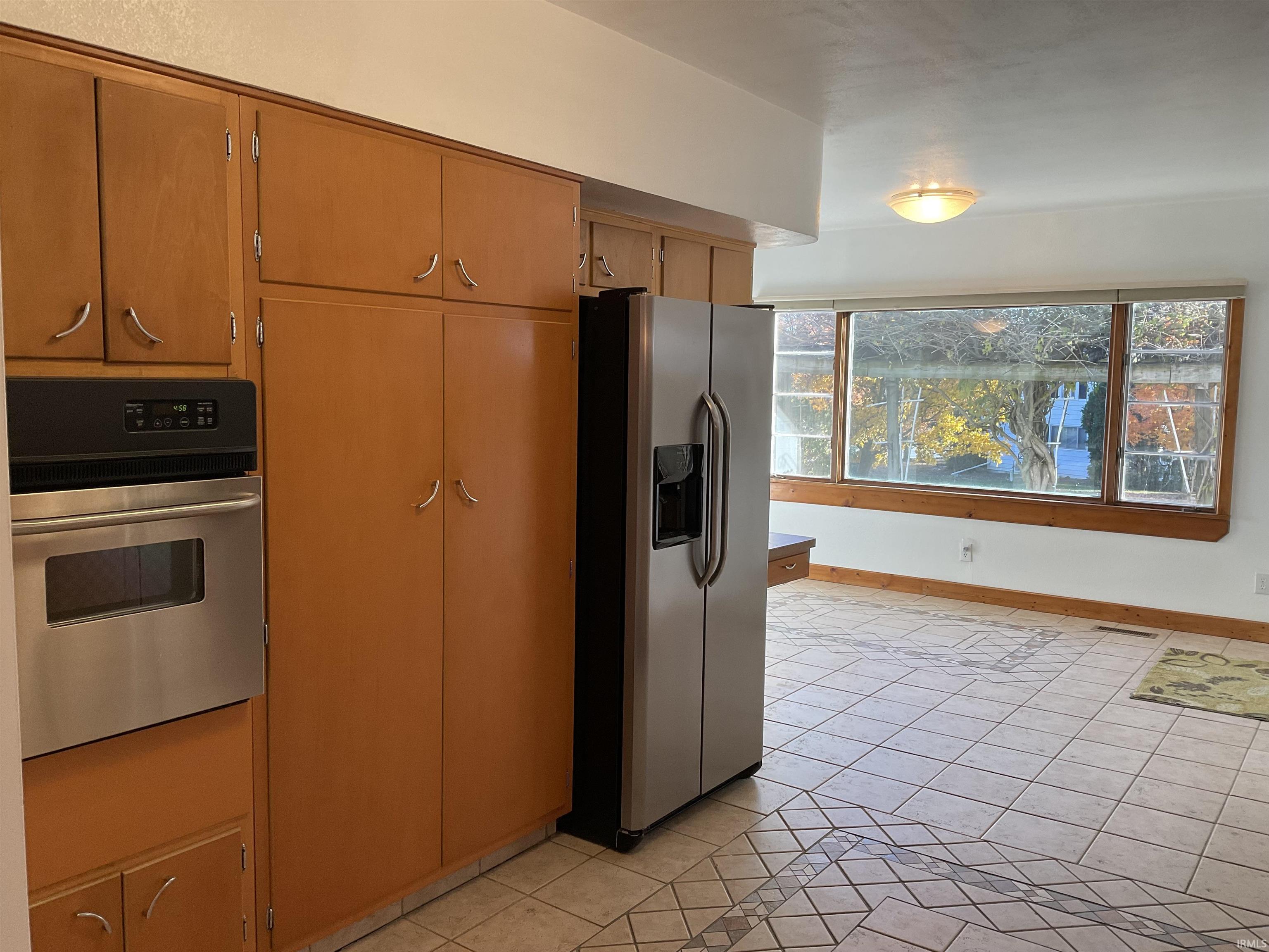 Kitchen with stainless steel appliances, light tile patterned flooring, and brown cabinetry