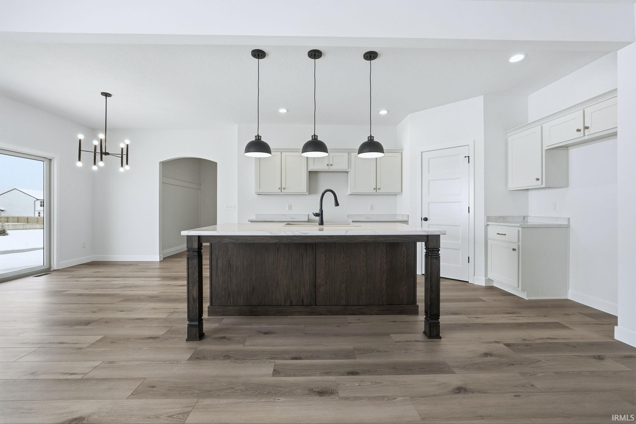 Kitchen featuring a breakfast bar, an island with sink, white cabinetry, decorative light fixtures, and recessed lighting