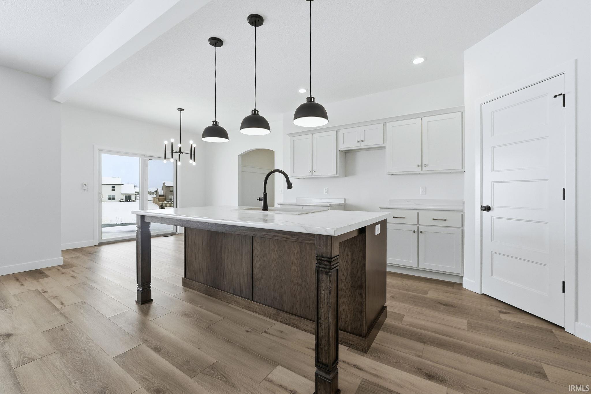 Kitchen featuring white cabinetry, dark brown cabinets, an island with sink, light wood finished floors, and pendant lighting