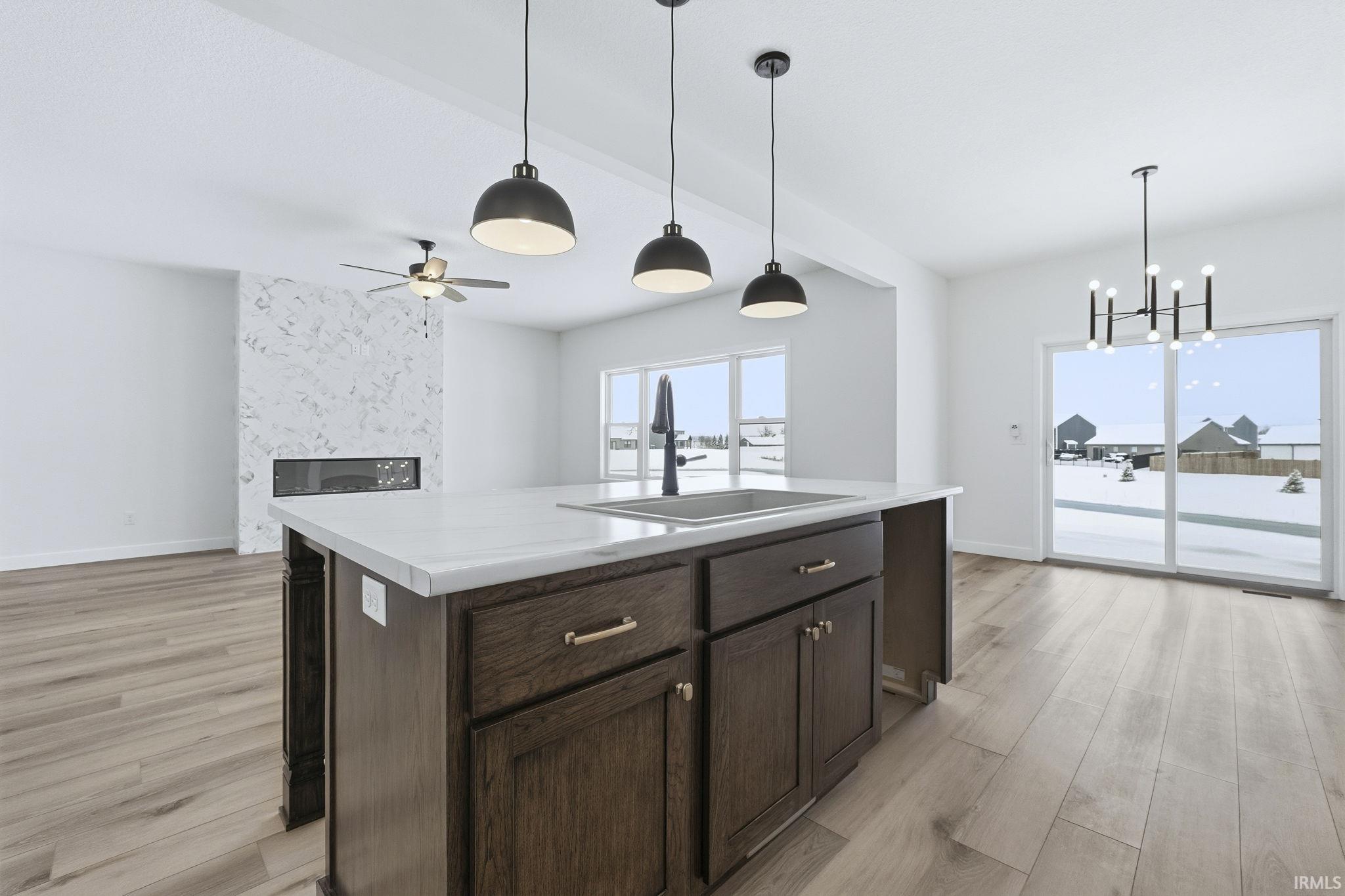 Kitchen with dark brown cabinets, an island with sink, light countertops, decorative light fixtures, and light wood finished floors