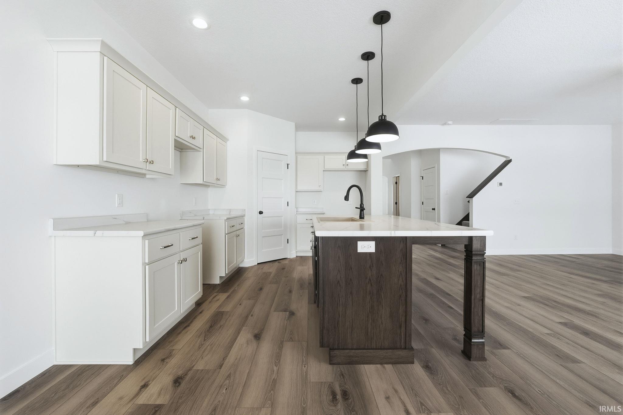 Kitchen featuring a kitchen breakfast bar, white cabinets, a kitchen island with sink, dark brown cabinetry, and decorative light fixtures
