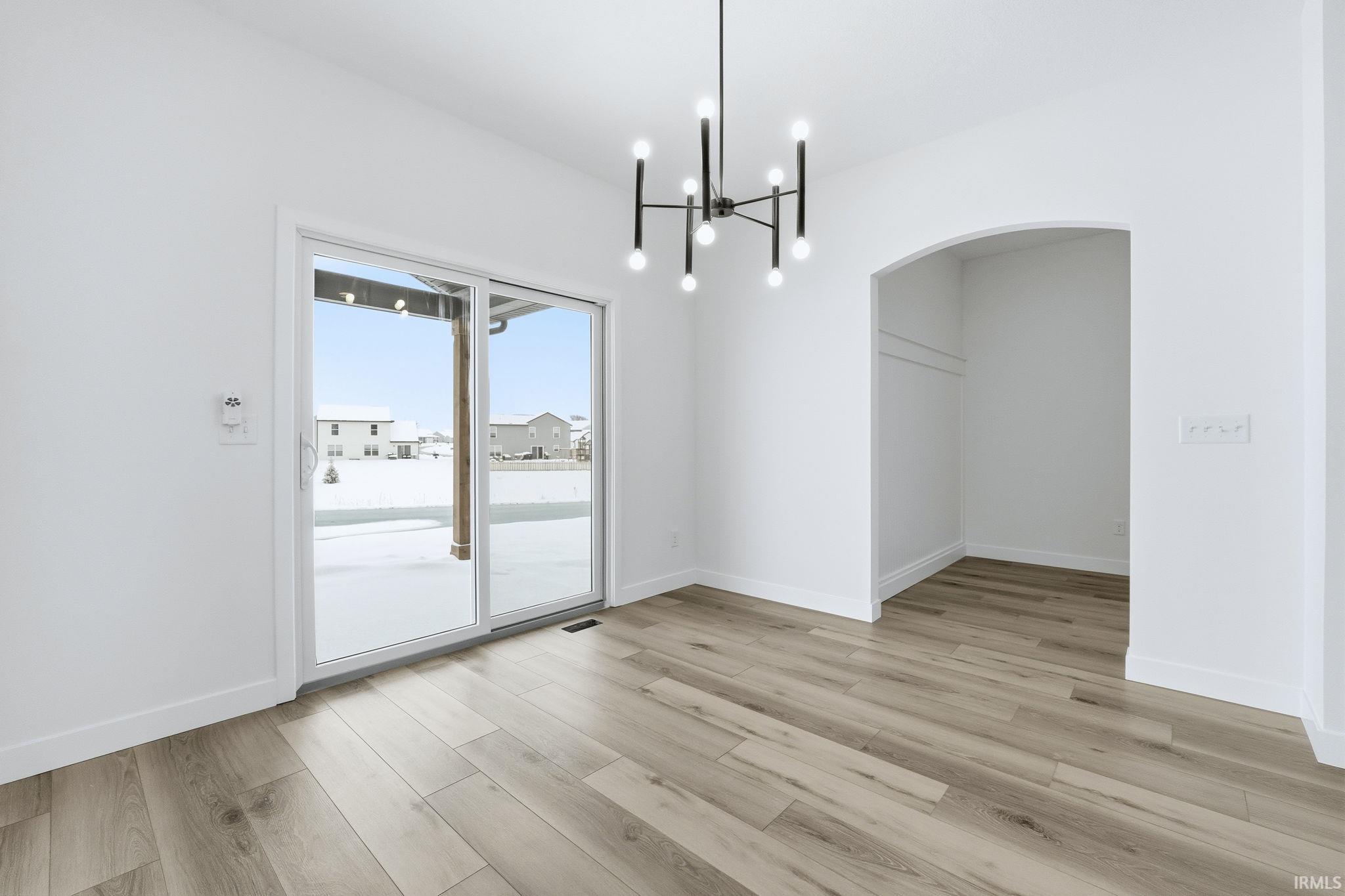 Unfurnished dining area with a chandelier, light wood finished floors, and arched walkways