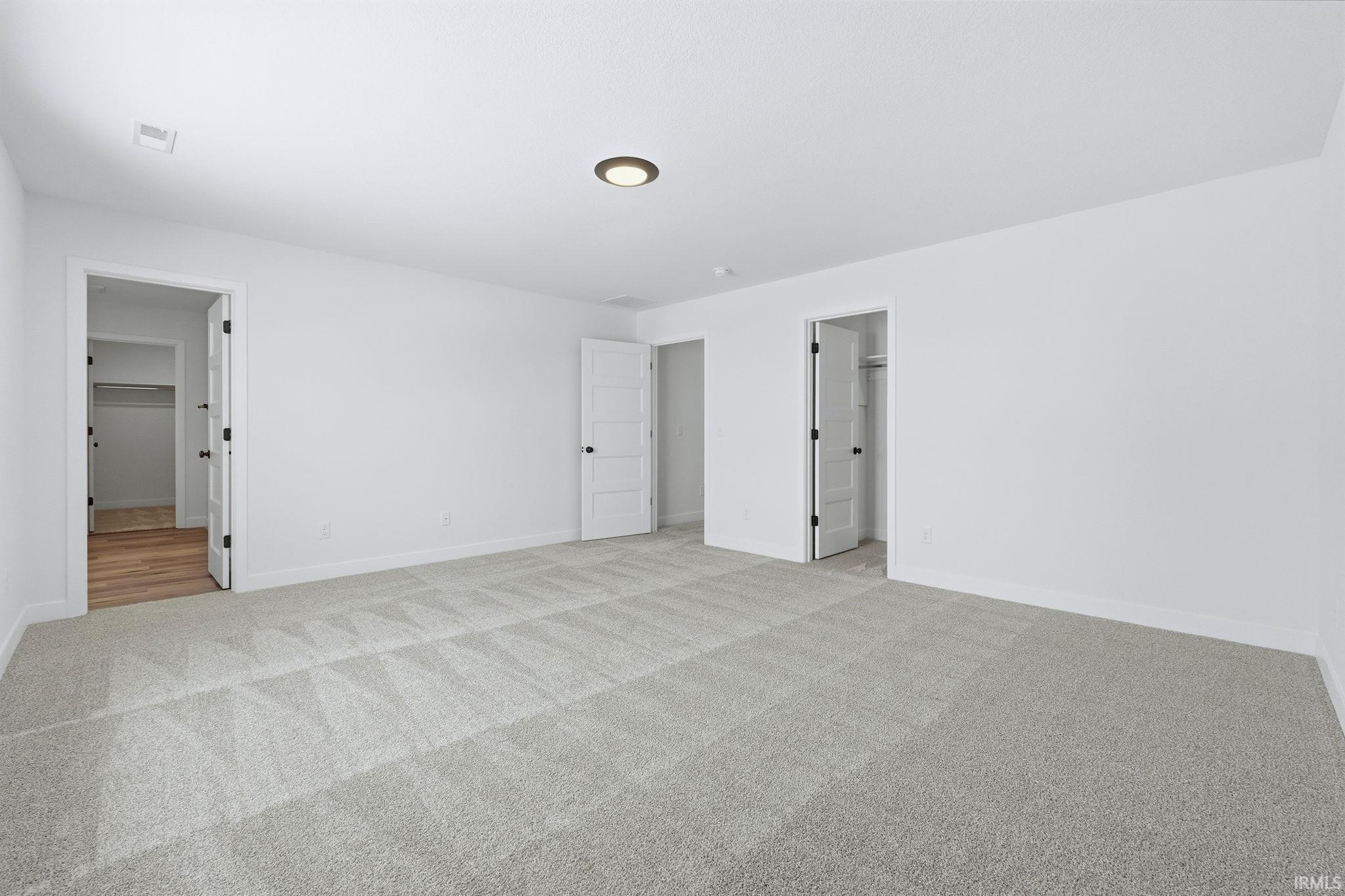 Unfurnished bedroom with light colored carpet, a spacious closet, and ensuite bath