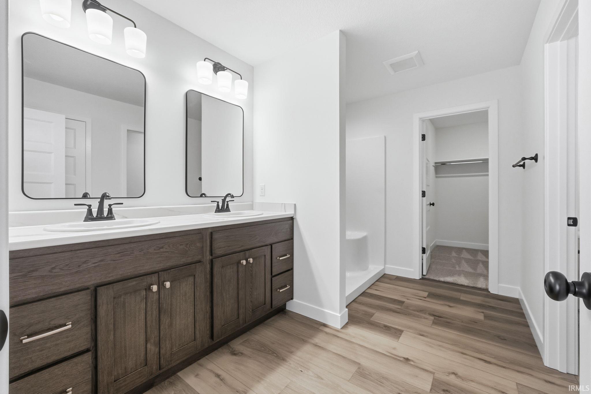Full bathroom featuring double vanity, a spacious closet, a stall shower, and light wood-style flooring