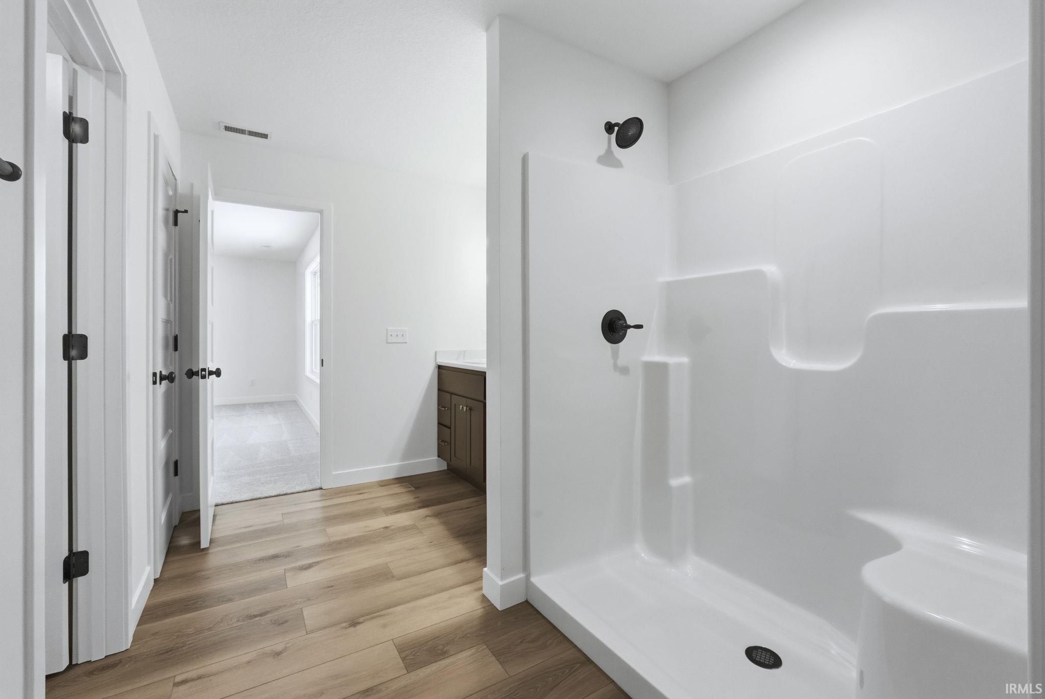 Full bath with vanity, light wood-style flooring, and a shower