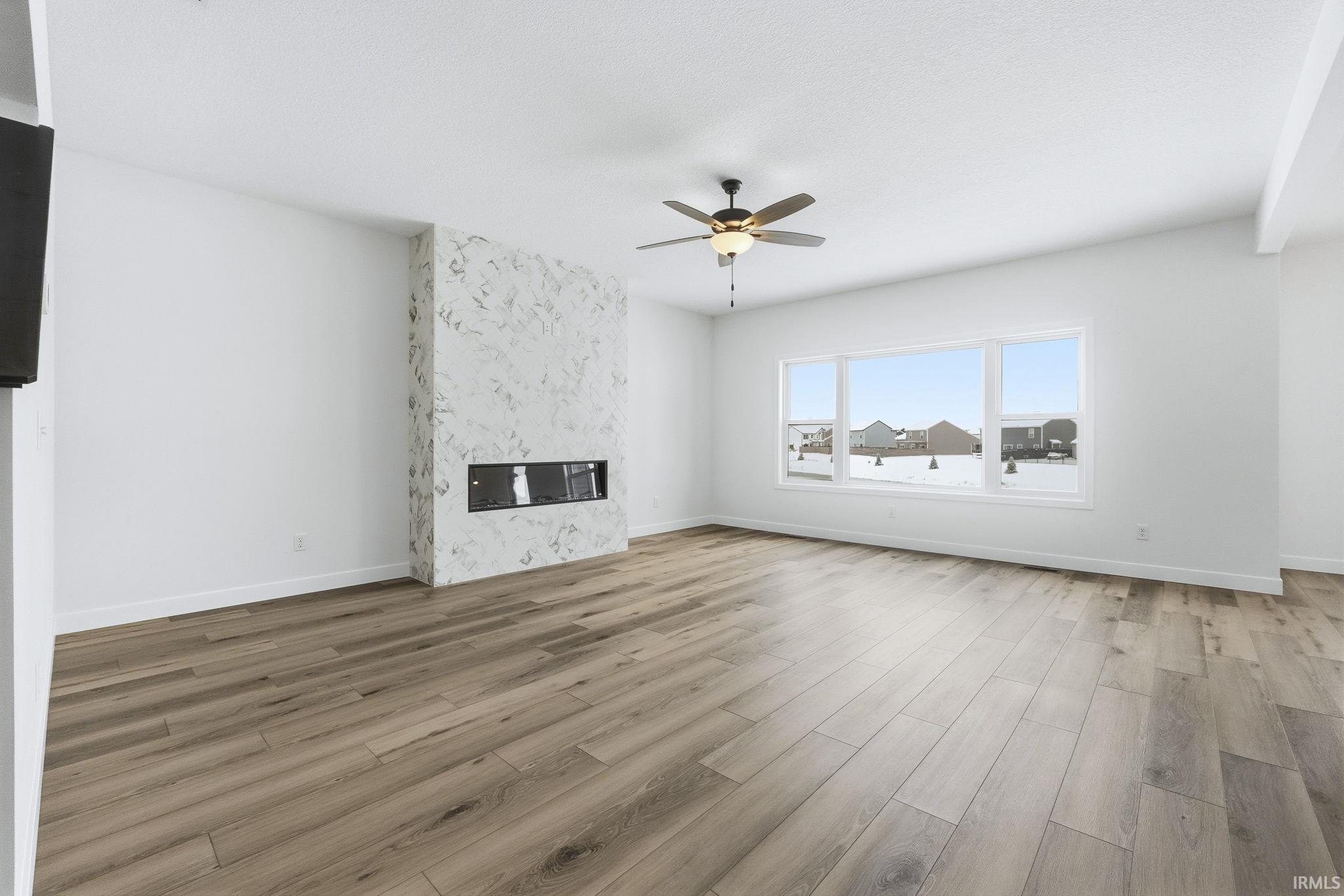 Unfurnished living room with a high end fireplace, light wood finished floors, and ceiling fan