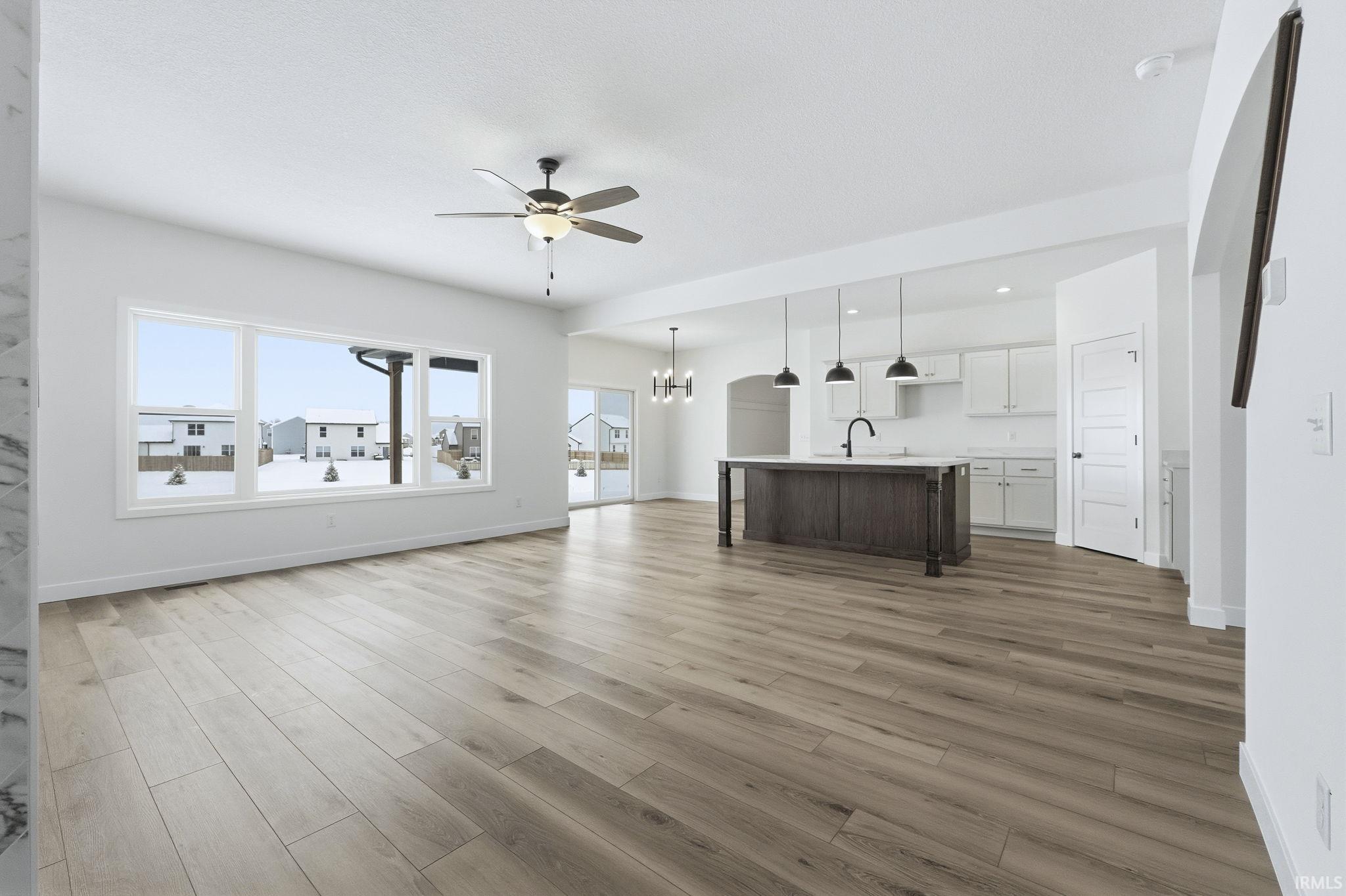 Unfurnished living room featuring a chandelier, light wood-style flooring, and a ceiling fan