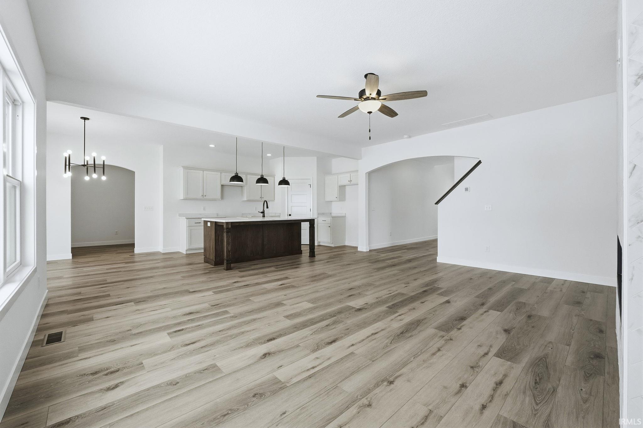 Unfurnished living room featuring arched walkways, a chandelier, light wood-style flooring, and a ceiling fan