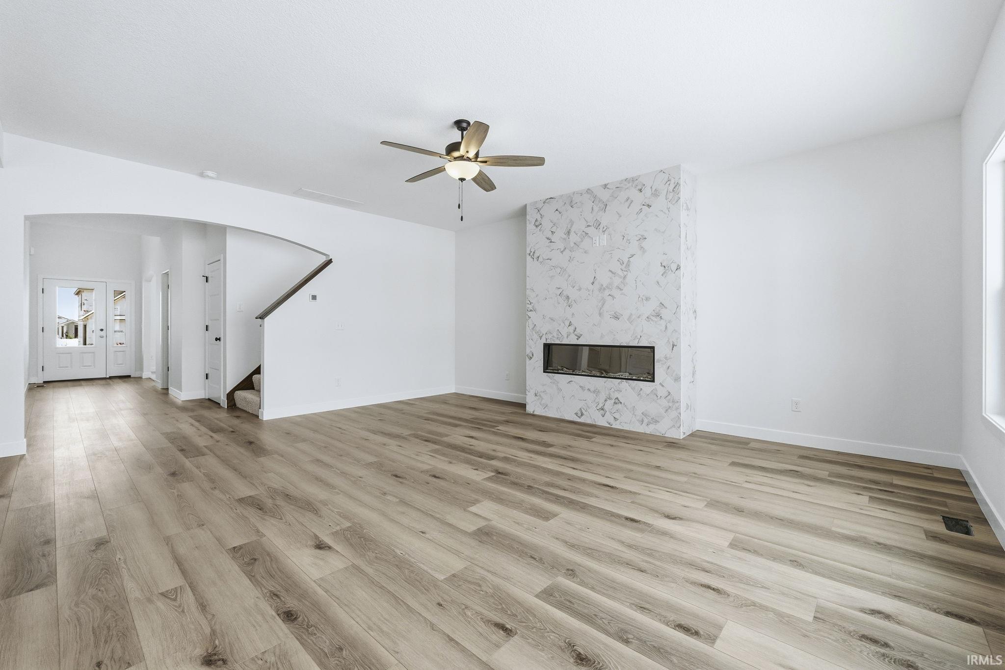 Unfurnished living room with light wood-type flooring, a high end fireplace, ceiling fan, stairs, and arched walkways