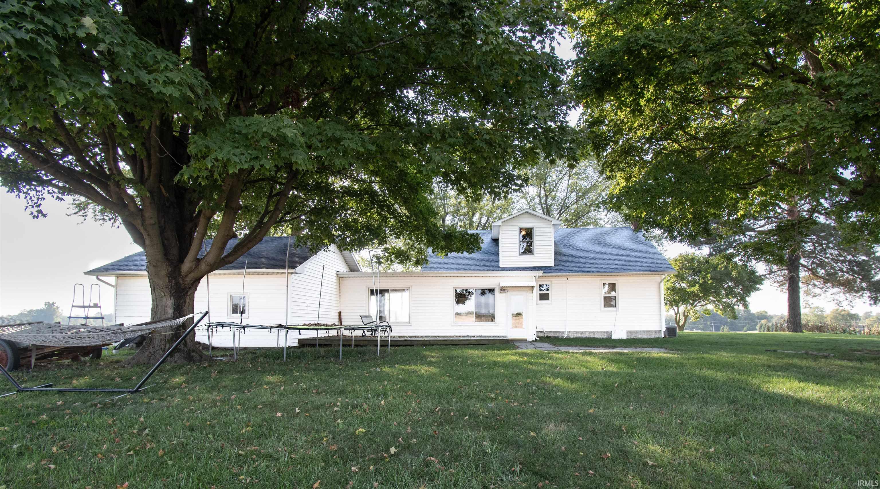 Rear view of house featuring a trampoline, a yard, and a shingled roof