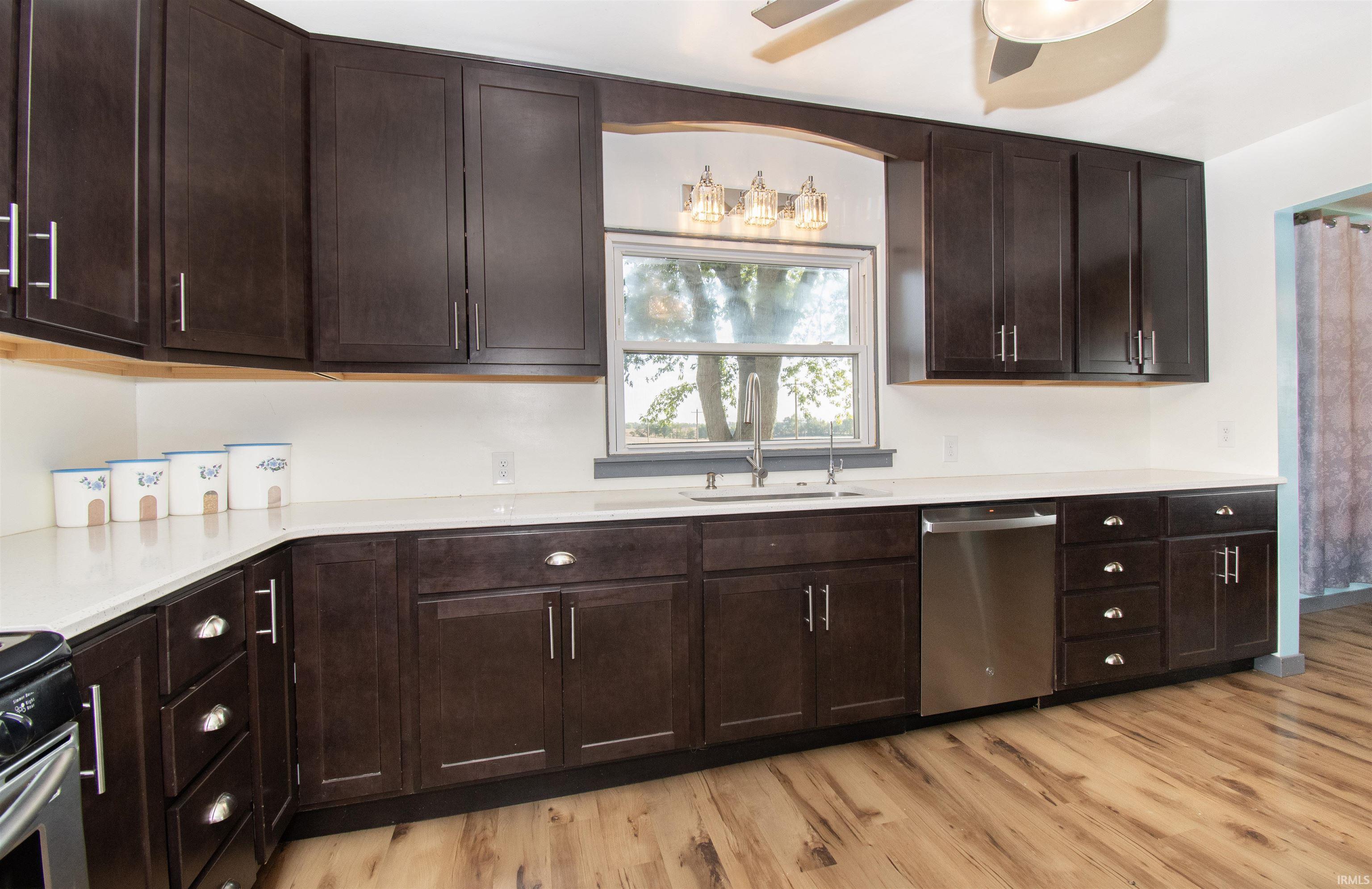 Kitchen with dark brown cabinets, stainless steel dishwasher, ceiling fan, light wood finished floors, and light stone countertops