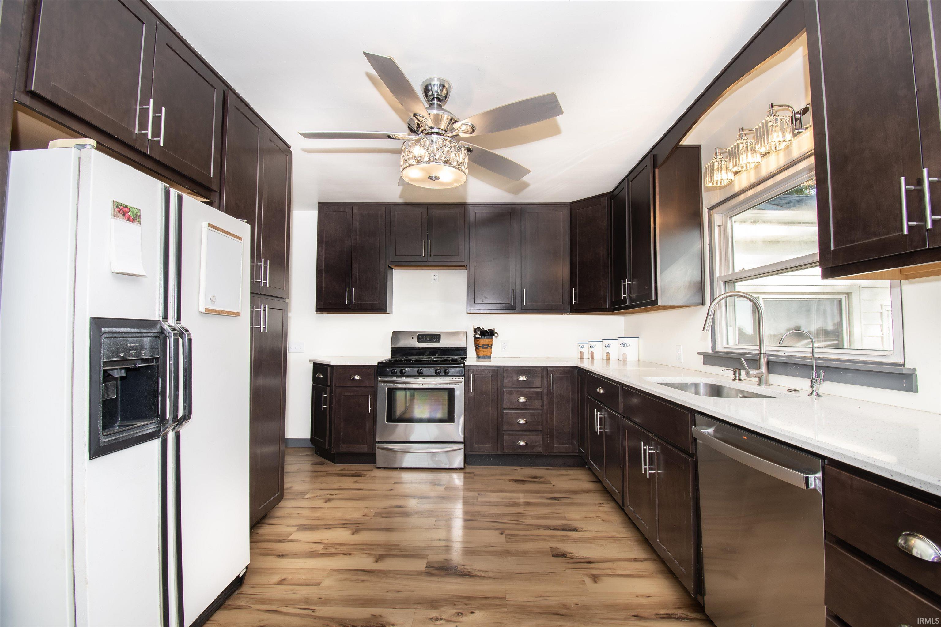 Kitchen with stainless steel appliances, dark brown cabinetry, light wood-style floors, light stone counters, and ceiling fan