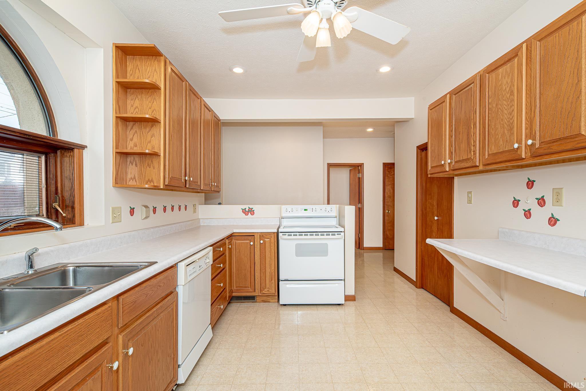 Kitchen with open shelves, white appliances, light countertops, brown cabinets, and recessed lighting