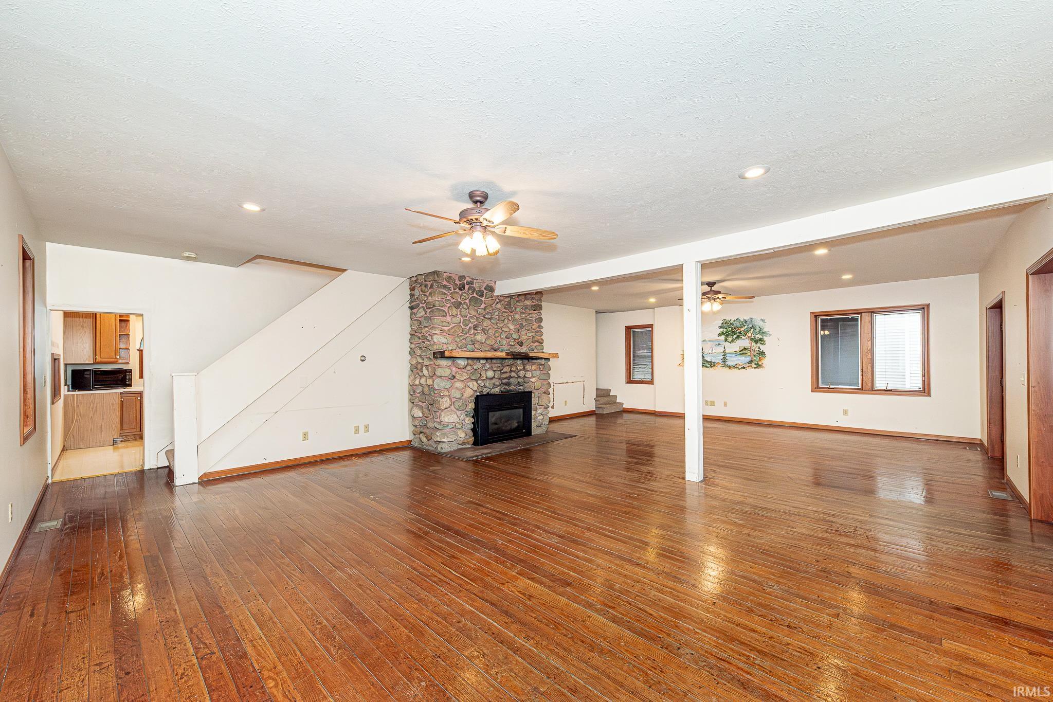 Unfurnished living room with ceiling fan, a stone fireplace, recessed lighting, and hardwood / wood-style floors