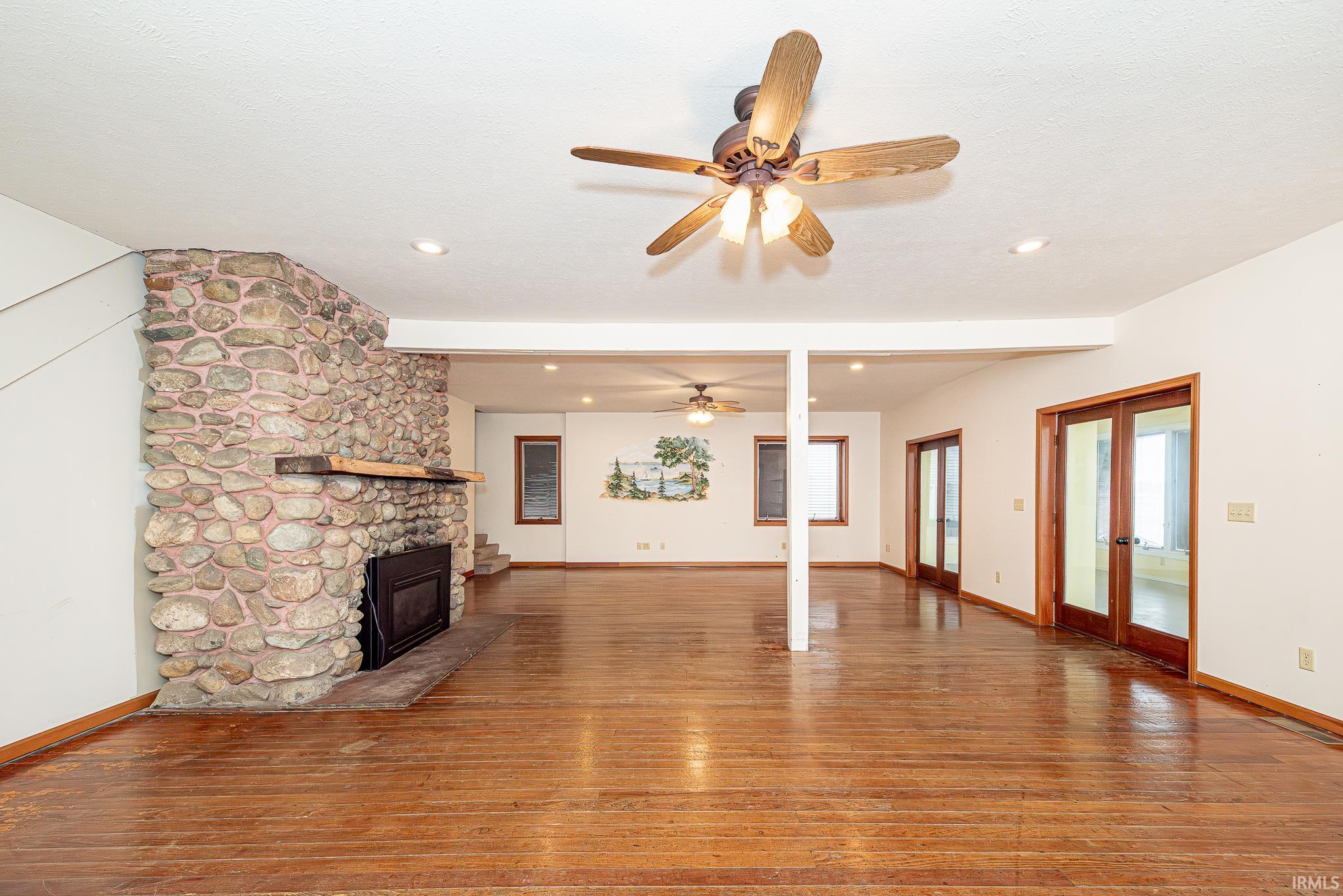 Unfurnished living room featuring ceiling fan, light wood finished floors, a fireplace, recessed lighting, and french doors