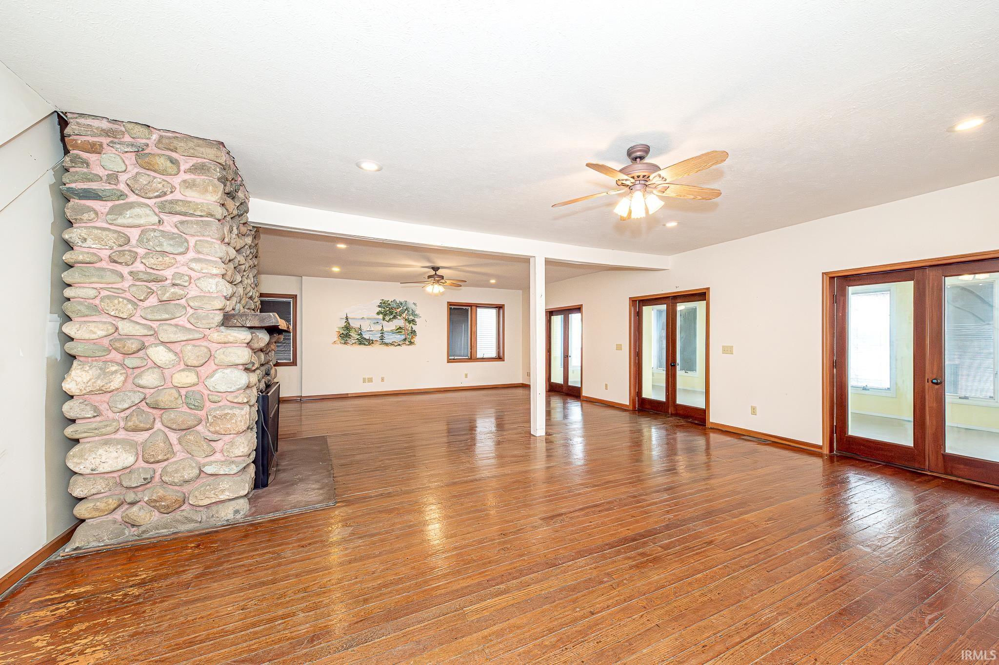 Unfurnished living room with french doors, ceiling fan, hardwood / wood-style floors, a stone fireplace, and recessed lighting