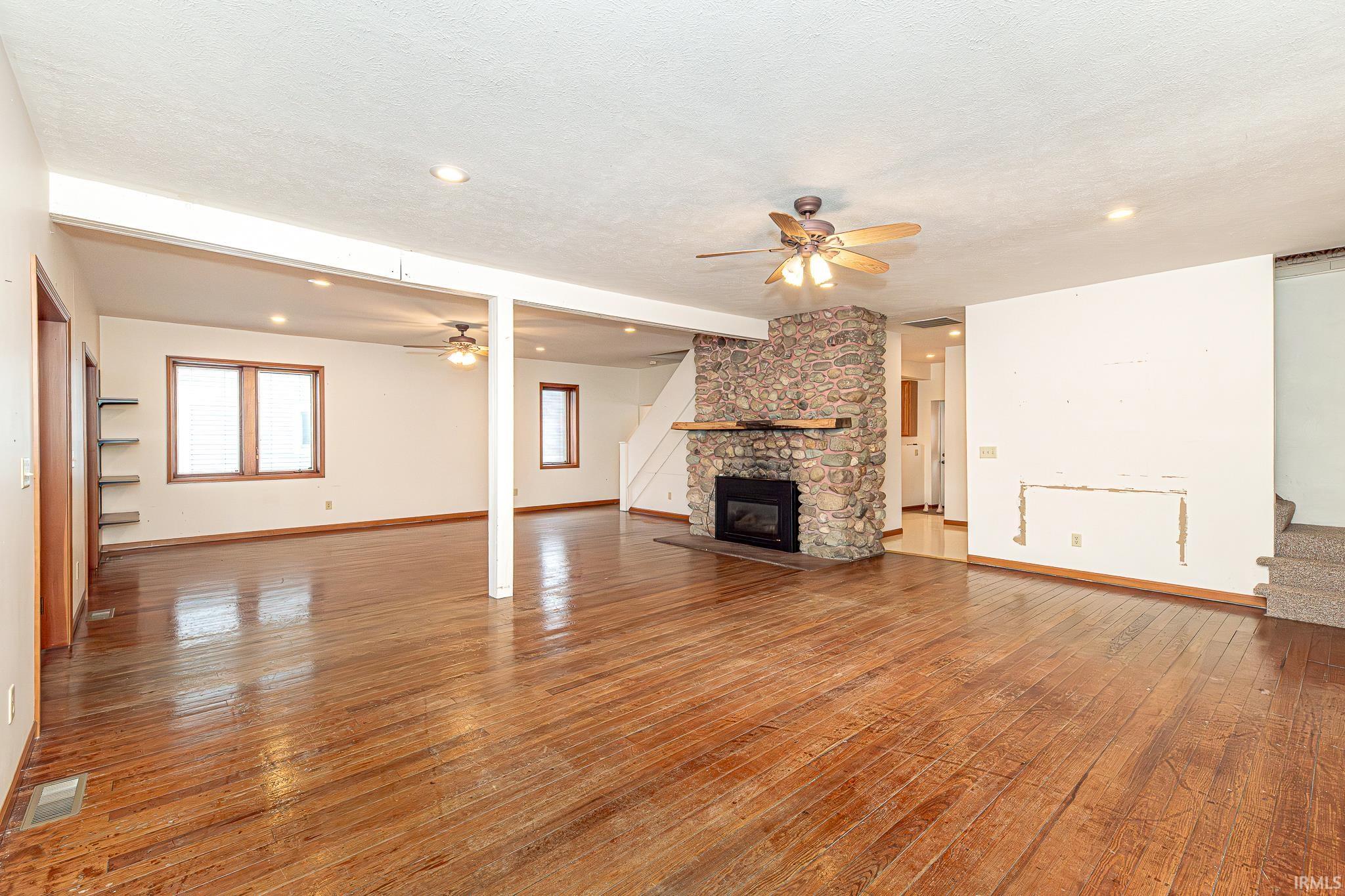 Unfurnished living room featuring a ceiling fan, stairs, a fireplace, light wood finished floors, and recessed lighting