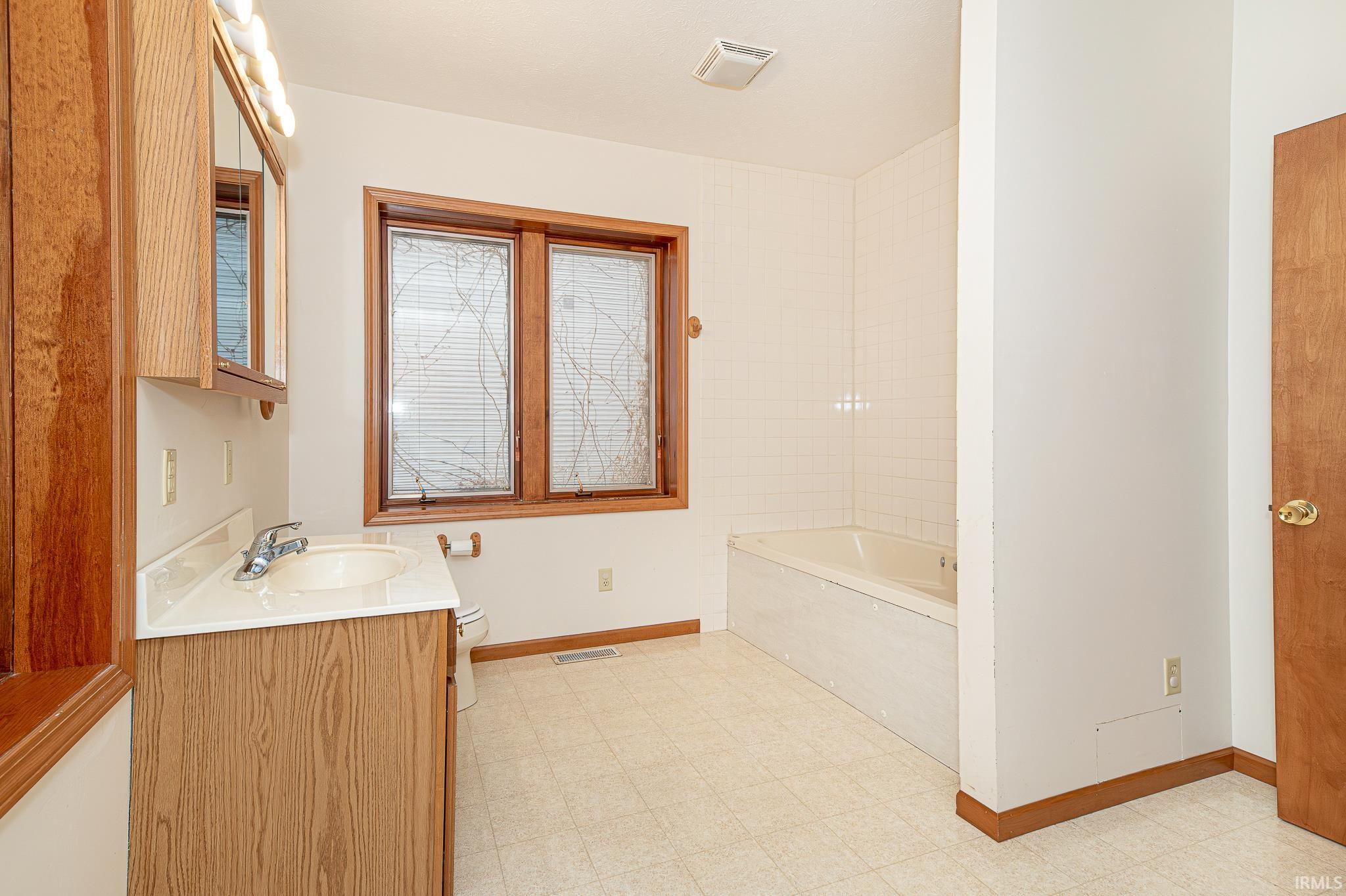 Full bathroom with a tub to relax in, vanity, and light floors