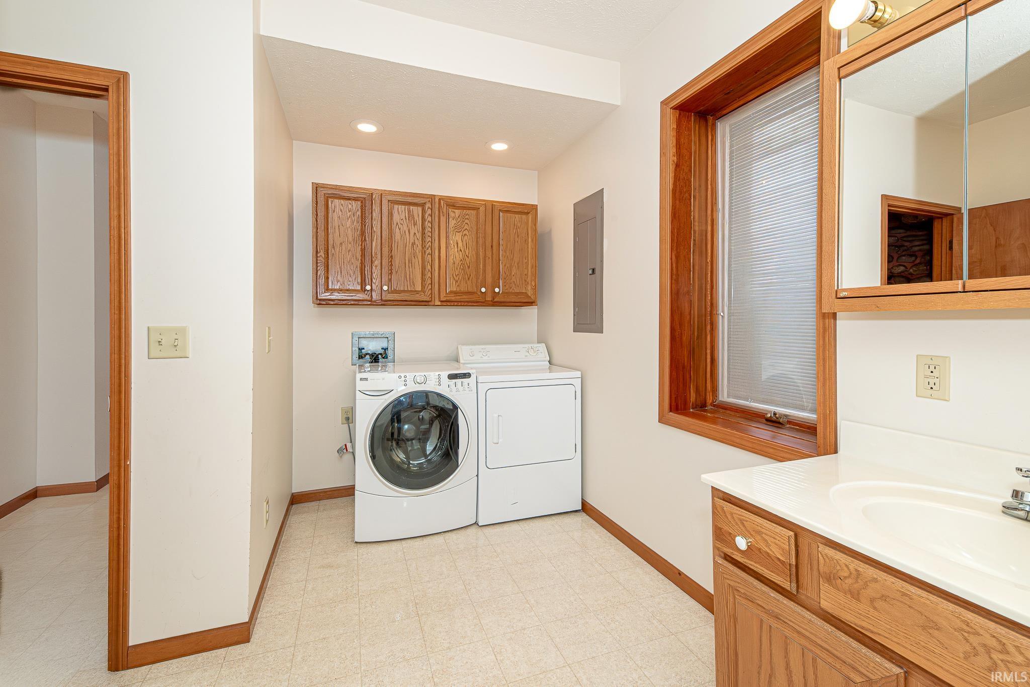 Laundry room with light floors, washing machine and clothes dryer, electric panel, and recessed lighting