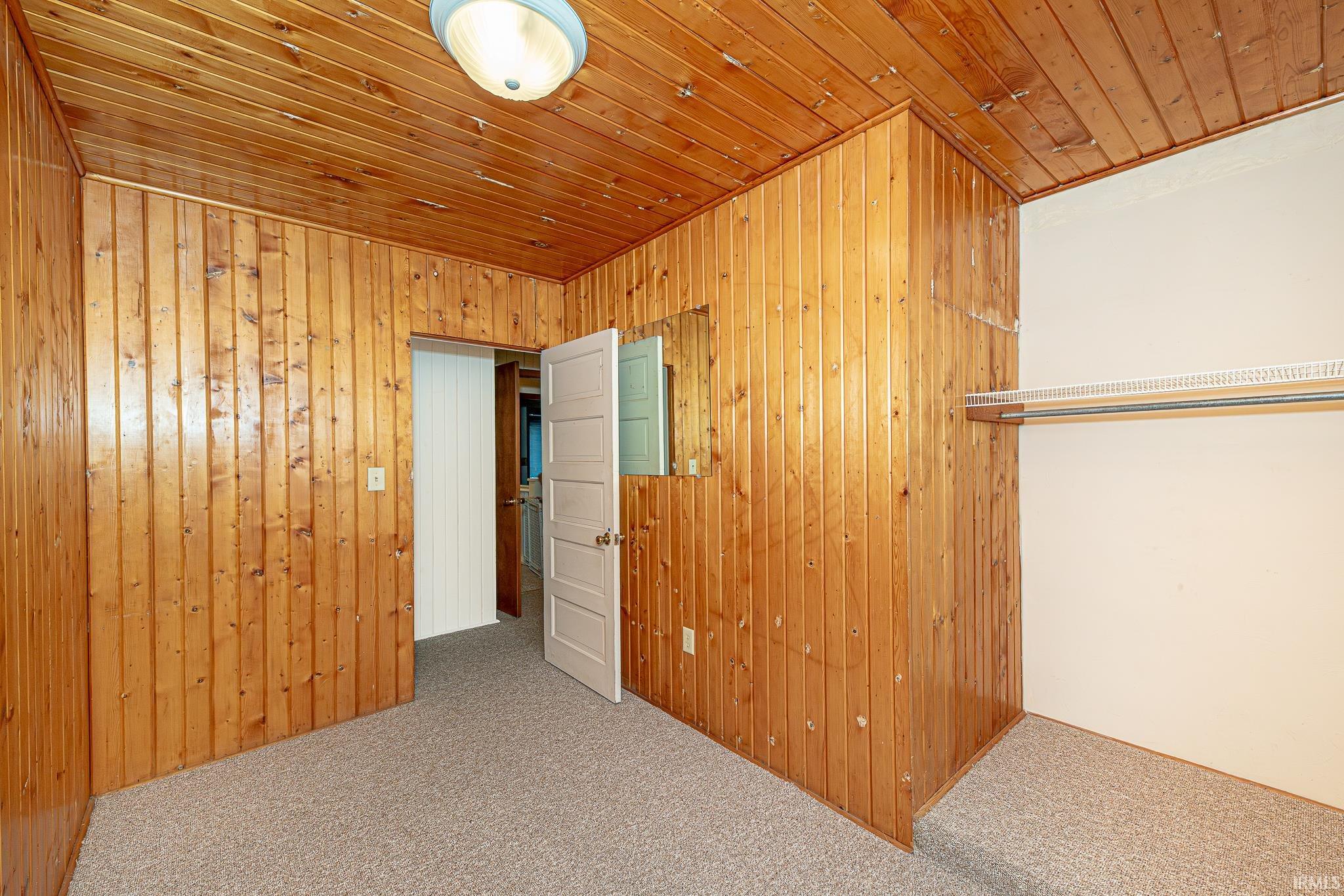 Unfurnished bedroom featuring carpet floors, wood ceiling, and wooden walls