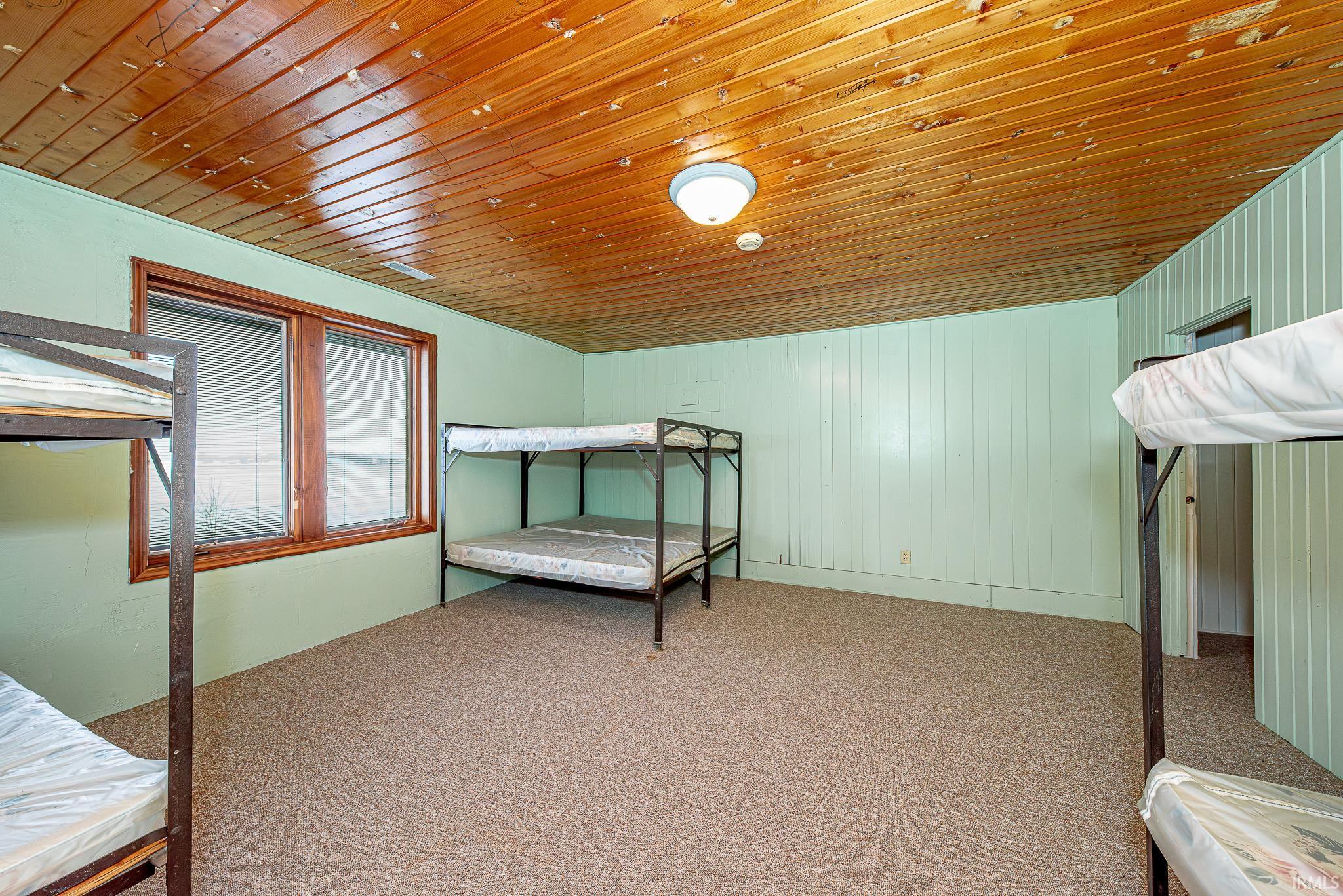 Unfurnished bedroom featuring wooden ceiling, carpet floors, and wood walls