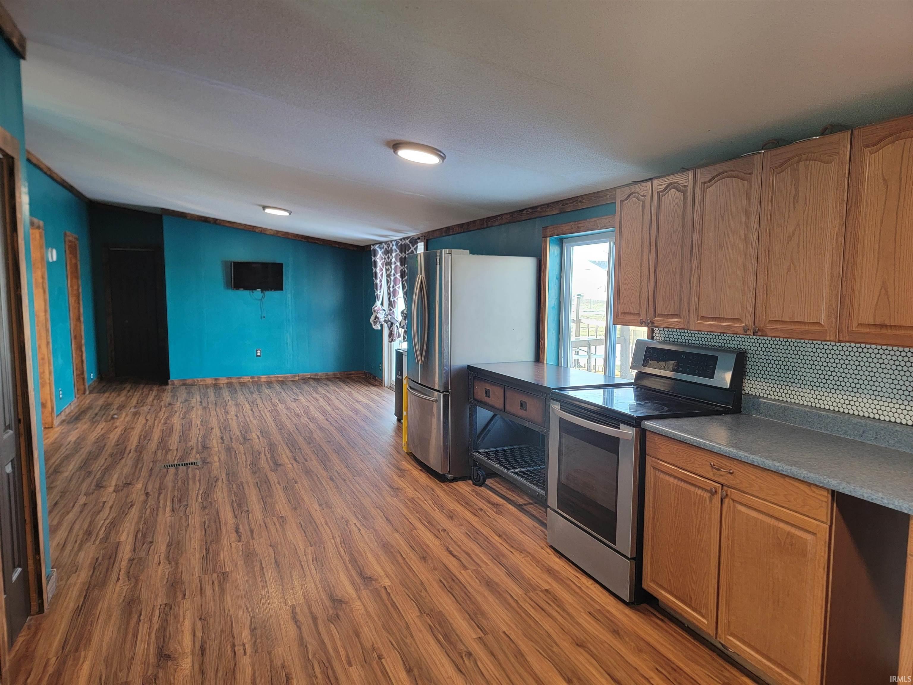Kitchen featuring appliances with stainless steel finishes, vaulted ceiling, dark wood-style flooring, brown cabinets, and dark countertops