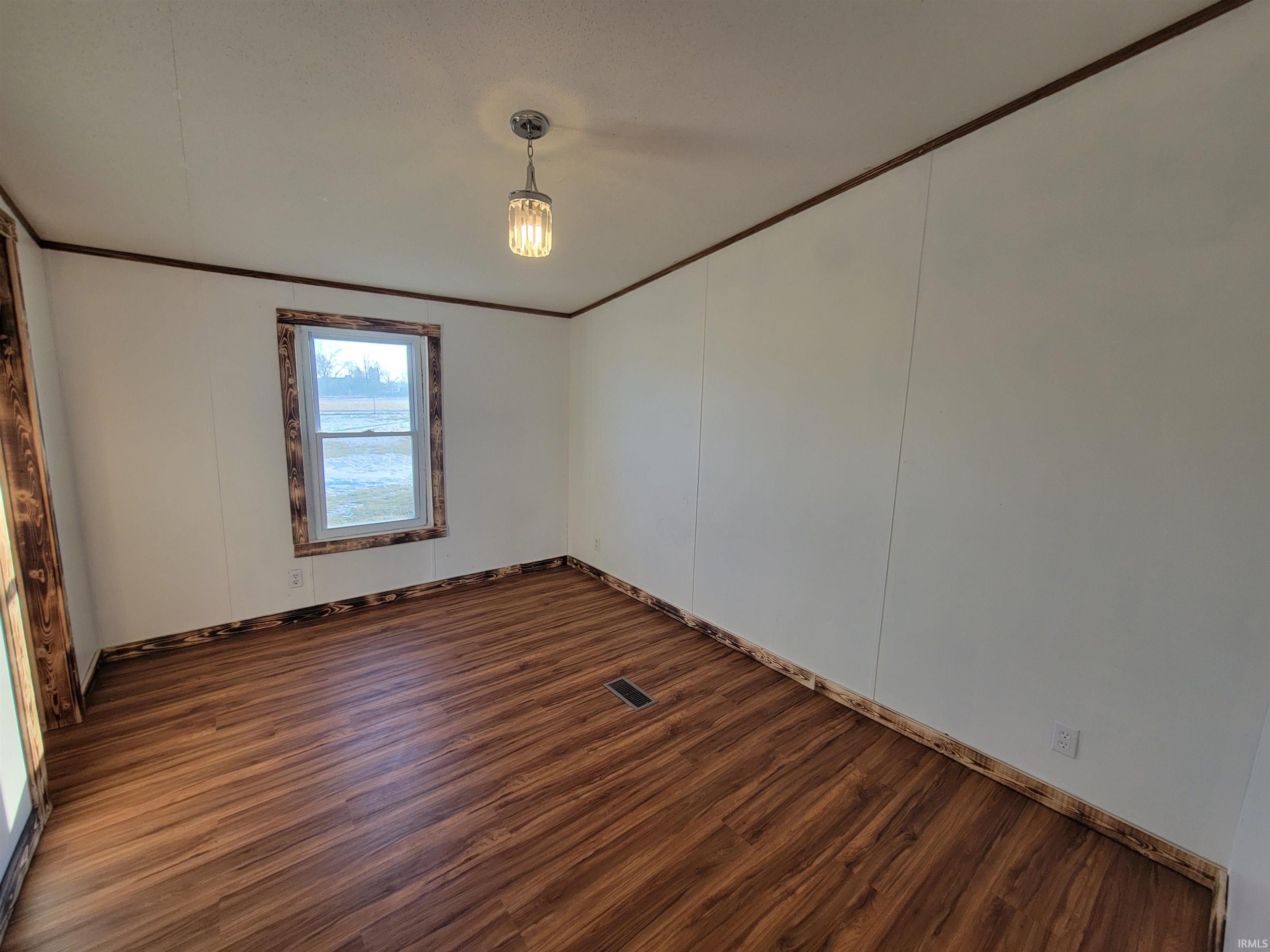 Spare room featuring dark wood finished floors and crown molding