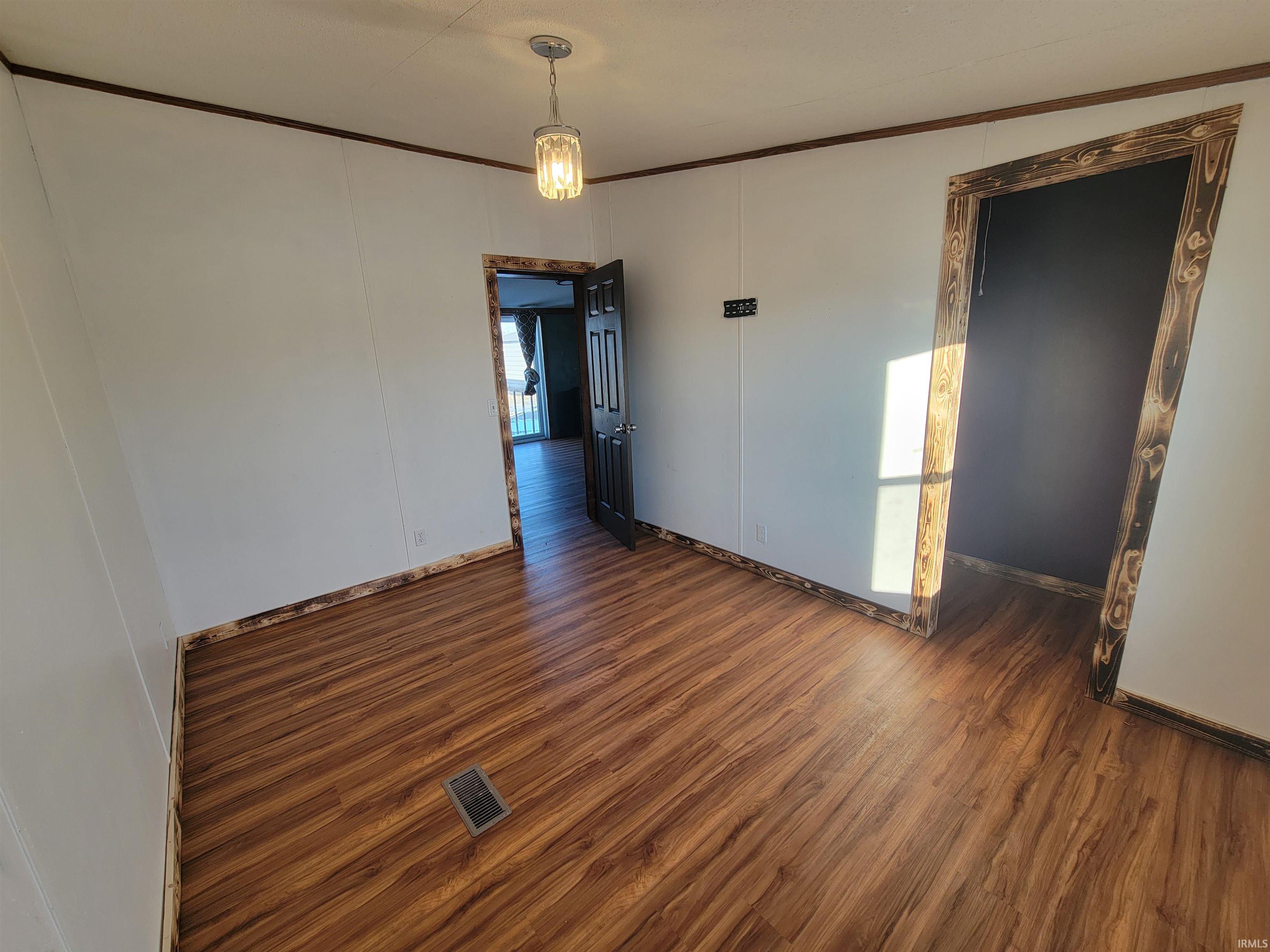 Empty room featuring wood finished floors, crown molding, and a decorative wall