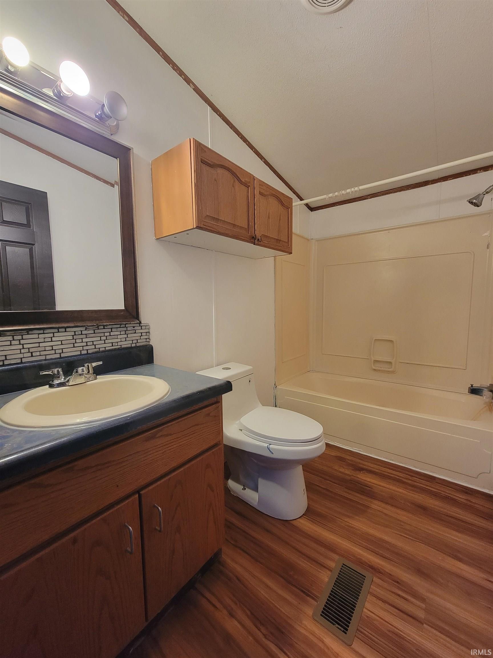 Full bath featuring vanity, shower / bath combination, dark wood-style flooring, and decorative backsplash