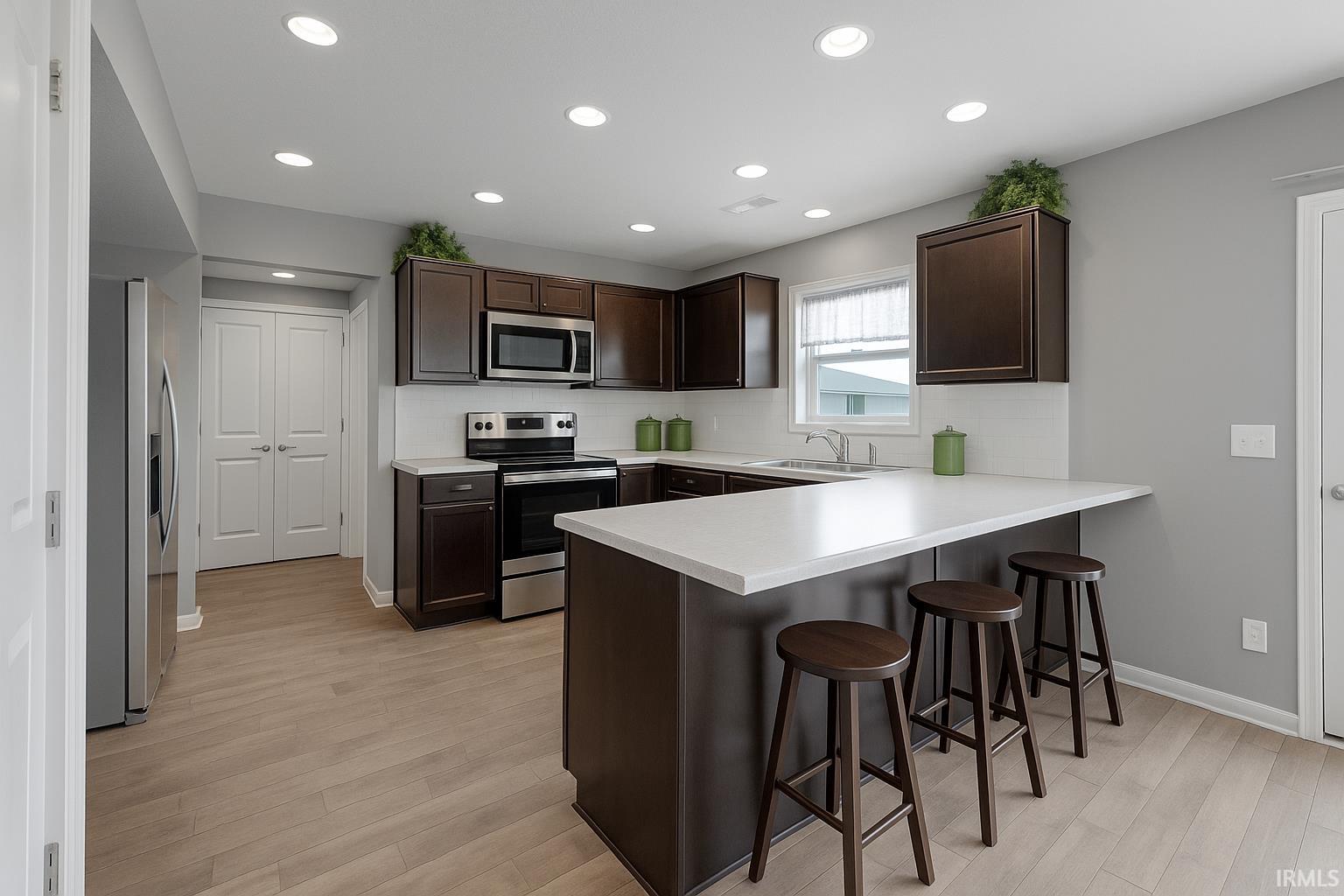 Kitchen with dark brown cabinetry, stainless steel appliances, decorative backsplash, light countertops, and a breakfast bar area