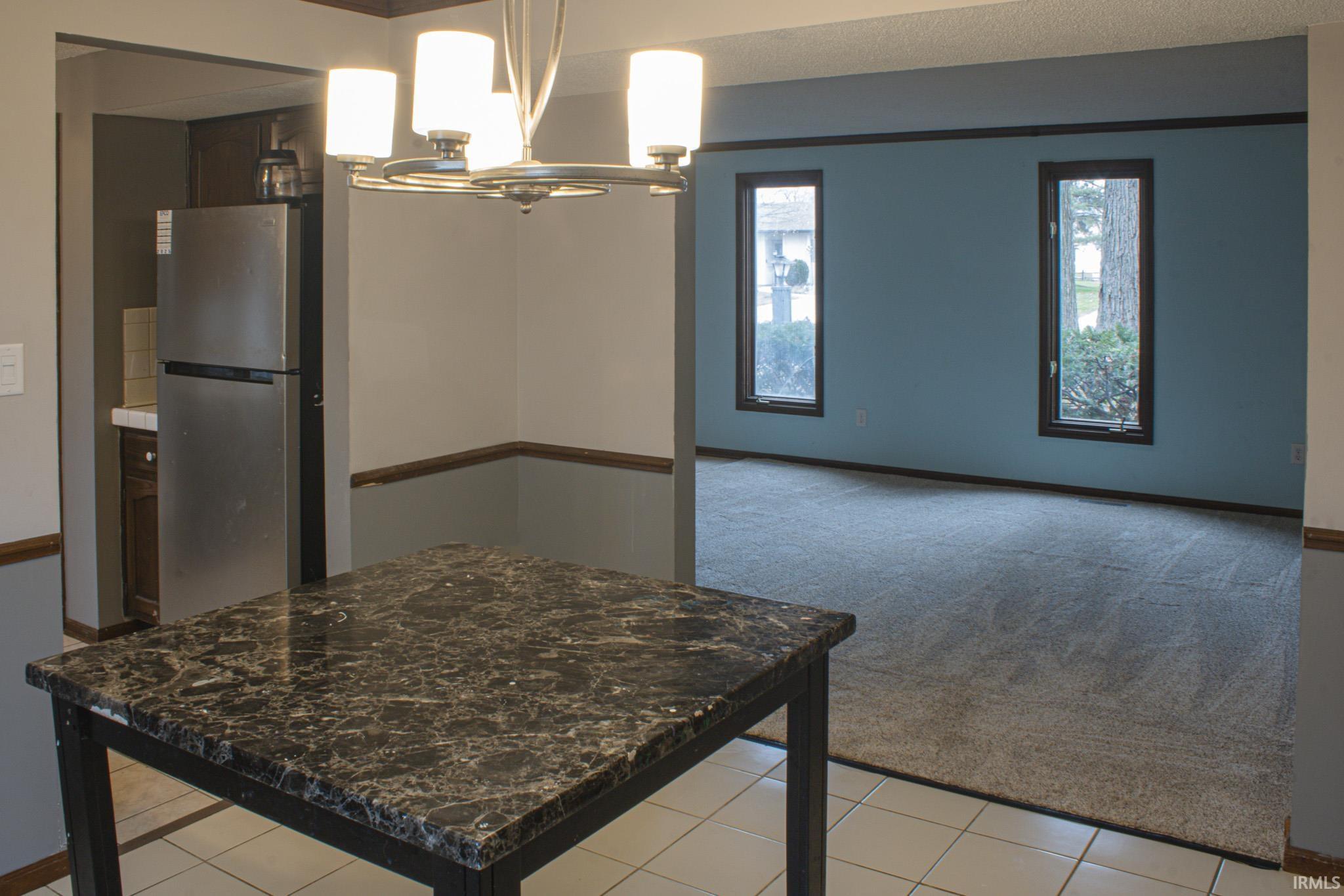 Kitchen featuring freestanding refrigerator, a chandelier, dark brown cabinetry, light carpet, and pendant lighting