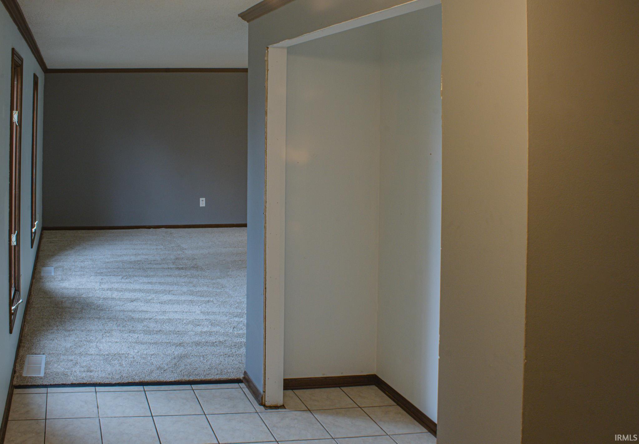 Hallway featuring light colored carpet, ornamental molding, and light tile patterned flooring