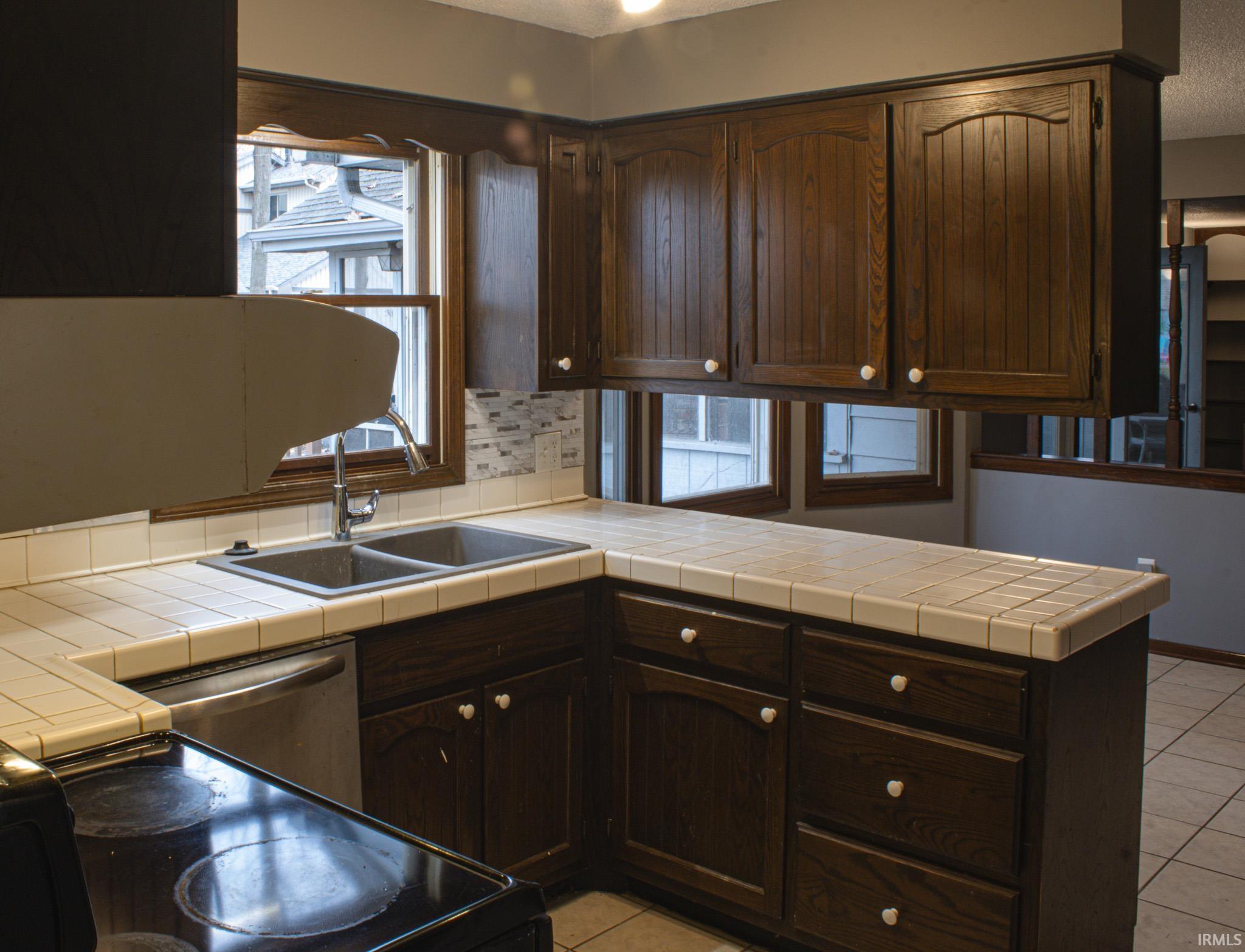 Kitchen featuring dark brown cabinets, healthy amount of natural light, tasteful backsplash, light tile patterned flooring, and a textured ceiling
