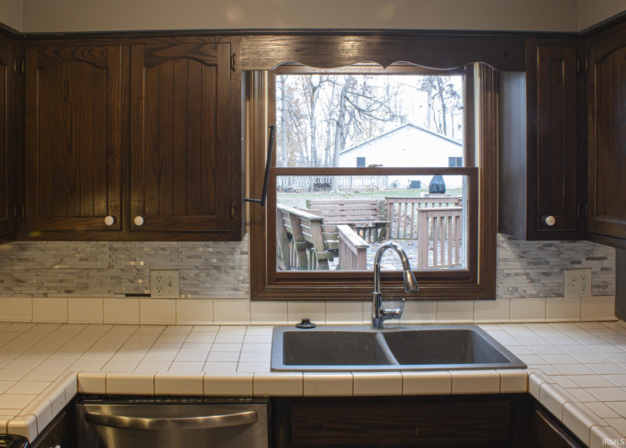 Kitchen with tile counters, dark brown cabinets, backsplash, and dishwasher