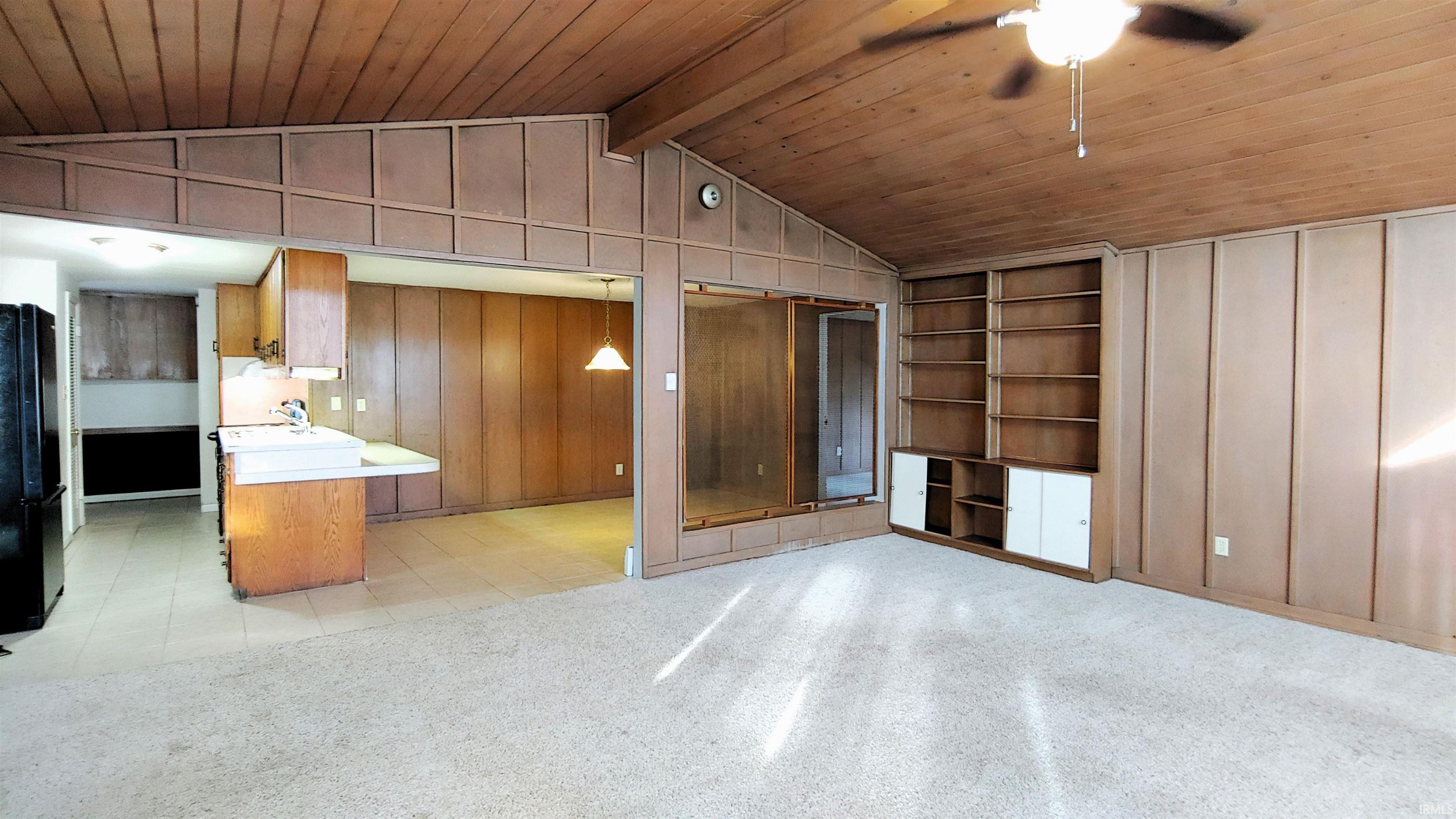 Family room with built in features, wood walls, a wood vaulted ceiling with exposed beams, and ceiling fan