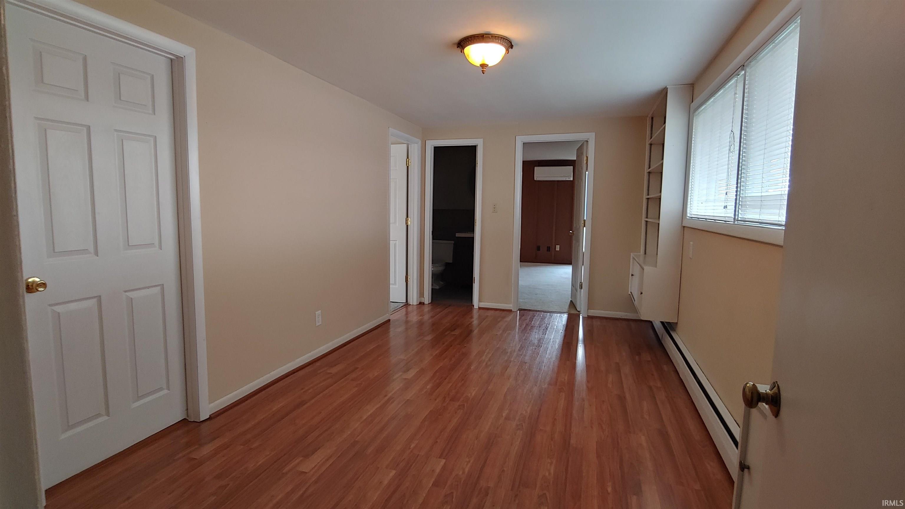 Unfurnished bedroom with a baseboard heating unit, light wood-style floors, and connected bathroom