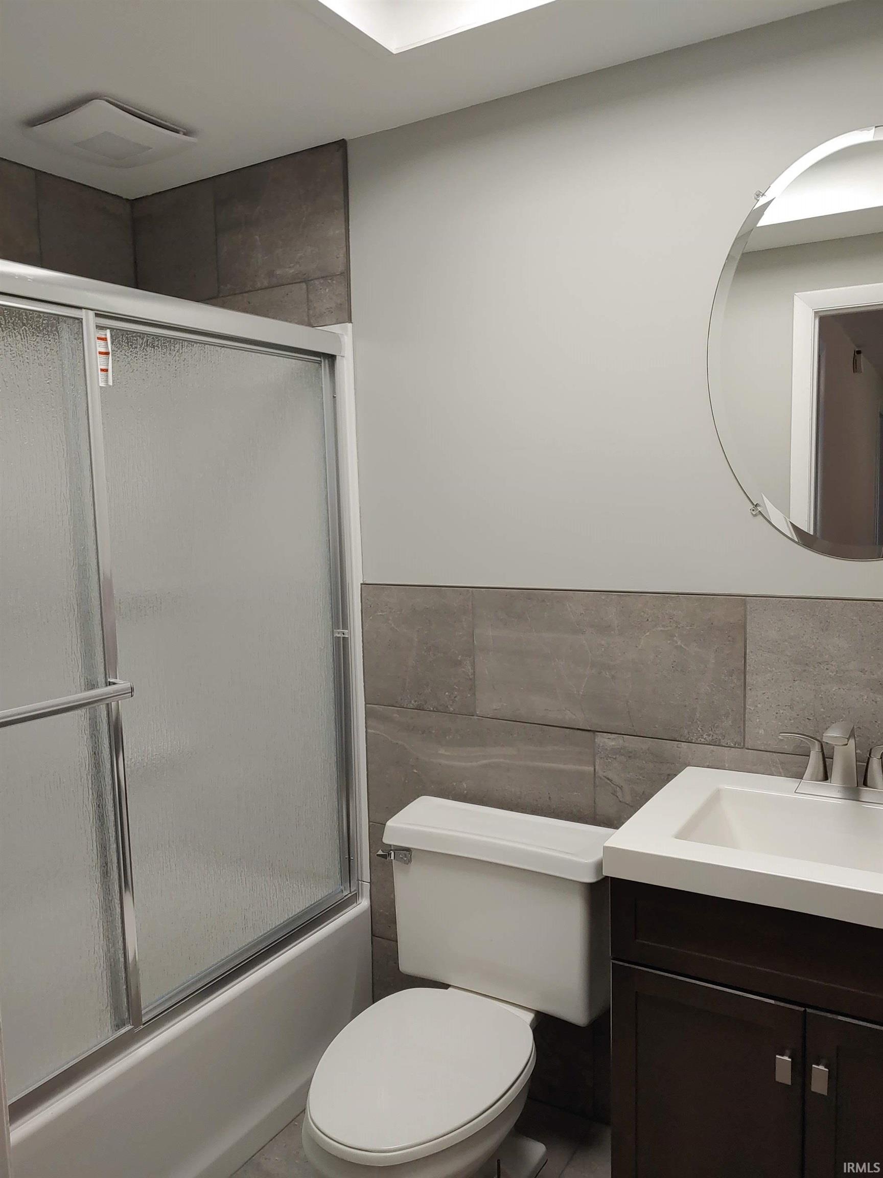 Full bath with tile walls, vanity, combined bath / shower with glass door