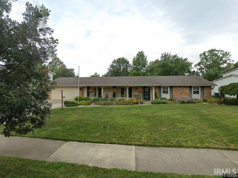 Ranch-style home featuring covered porch, a front yard, brick siding, and a garage