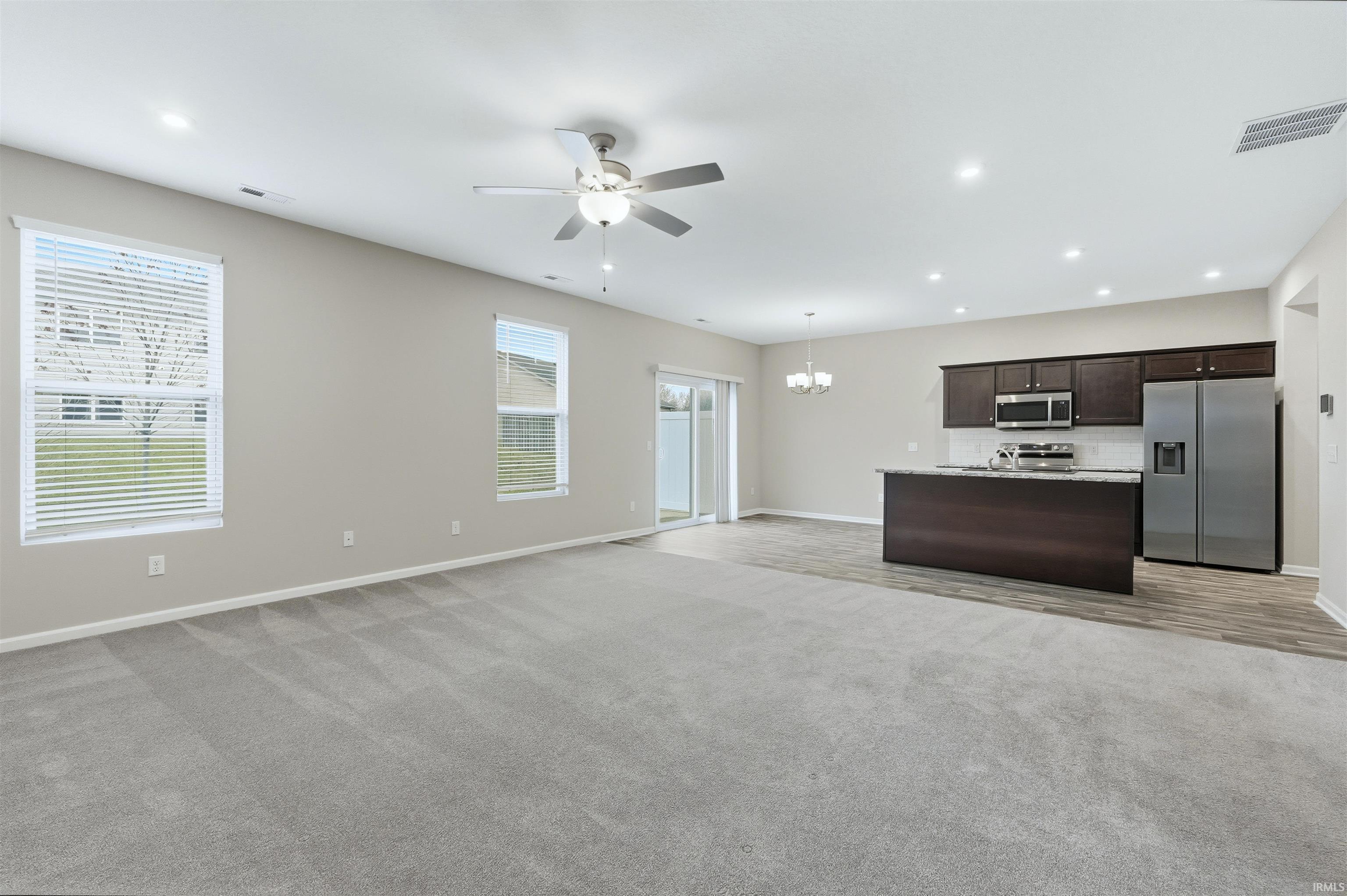 Kitchen featuring open floor plan, dark brown cabinetry, appliances with stainless steel finishes, a kitchen island with sink, and light carpet