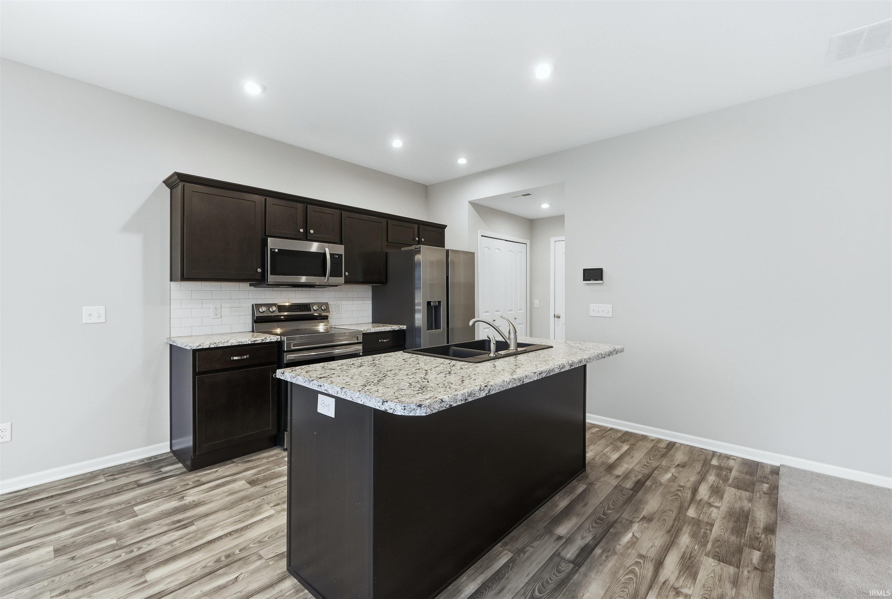 Kitchen with a kitchen island with sink, backsplash, stainless steel appliances, recessed lighting, and light vinyl plank flooring