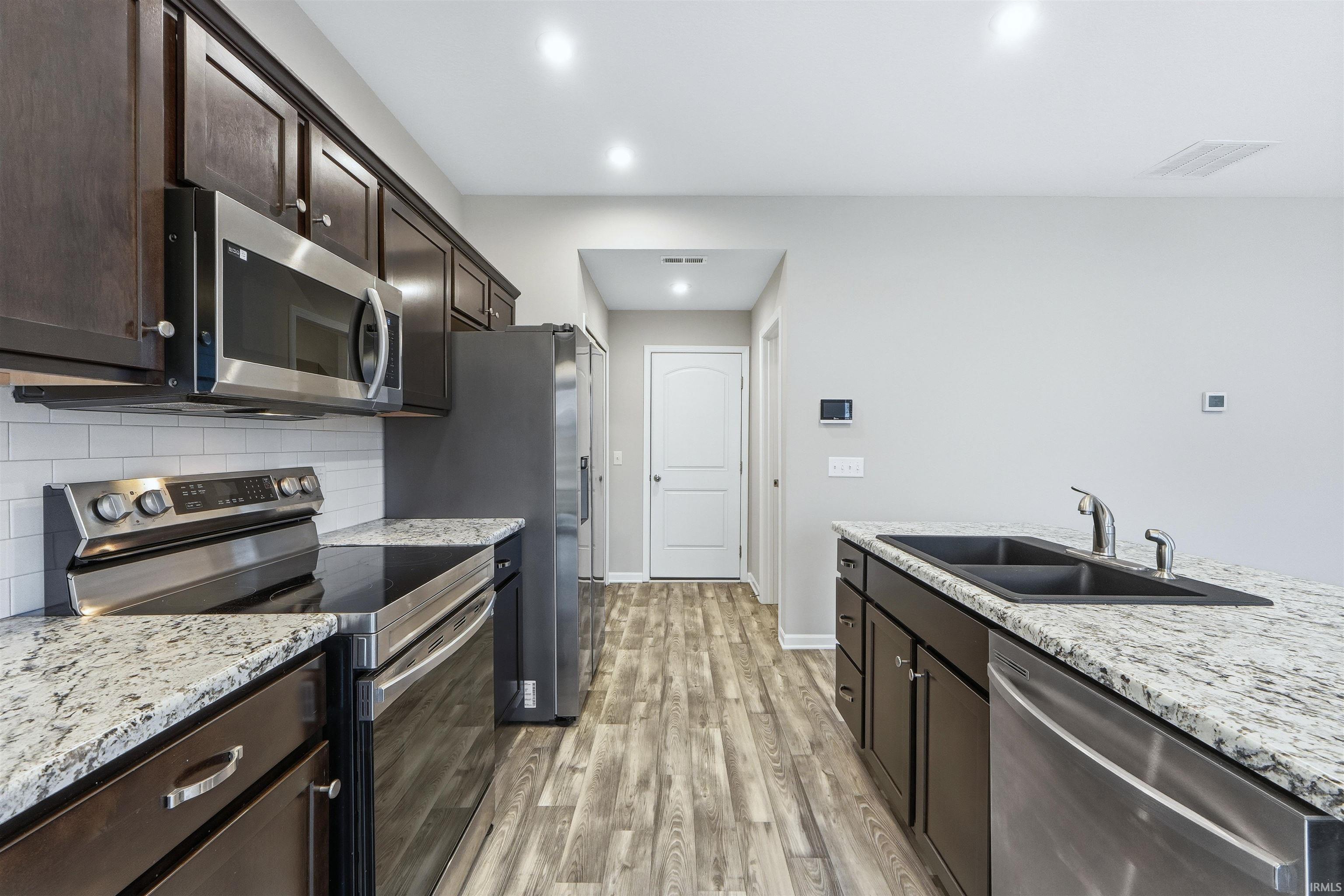 Kitchen featuring stainless steel appliances, dark brown cabinets, backsplash, light vinyl plank flooring