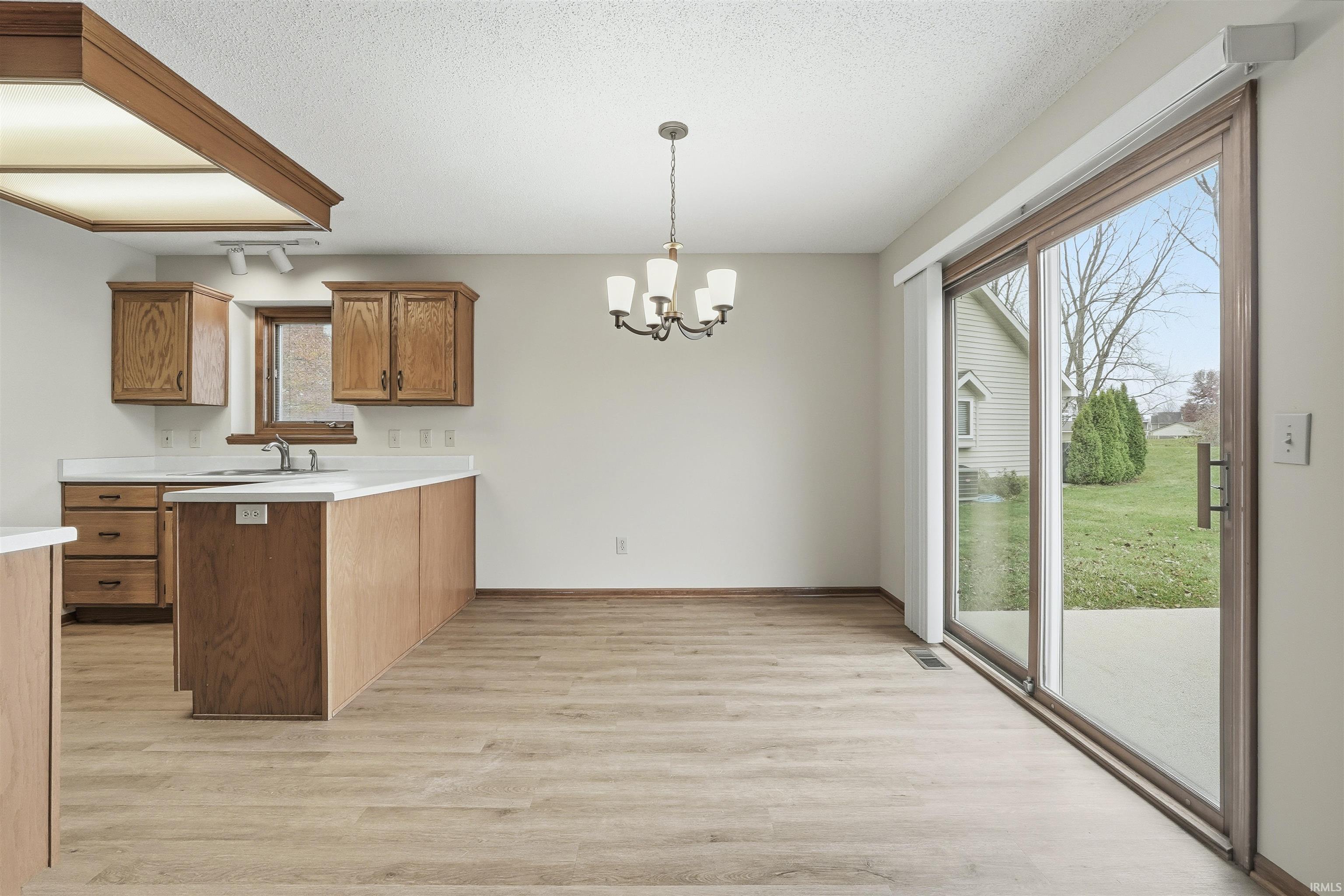 Kitchen with light countertops, a peninsula, brown cabinets, light wood-type flooring, and hanging light fixtures