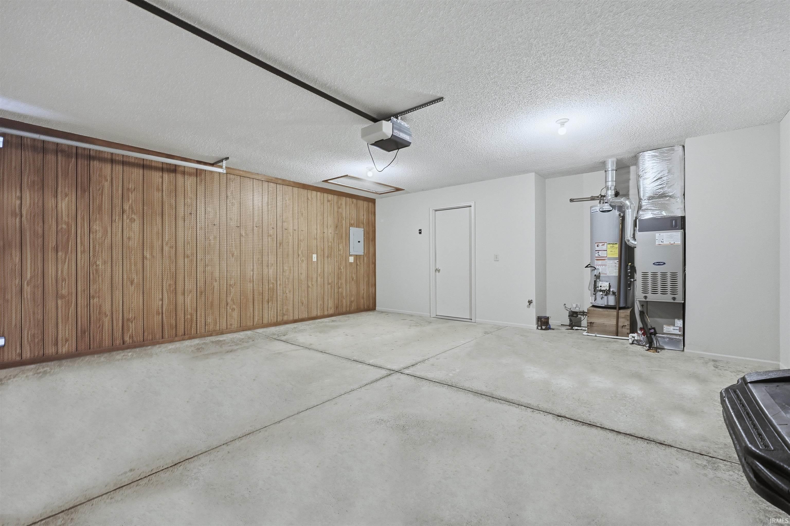 Garage featuring wooden walls, heating unit, water heater, electric panel, and a garage door opener